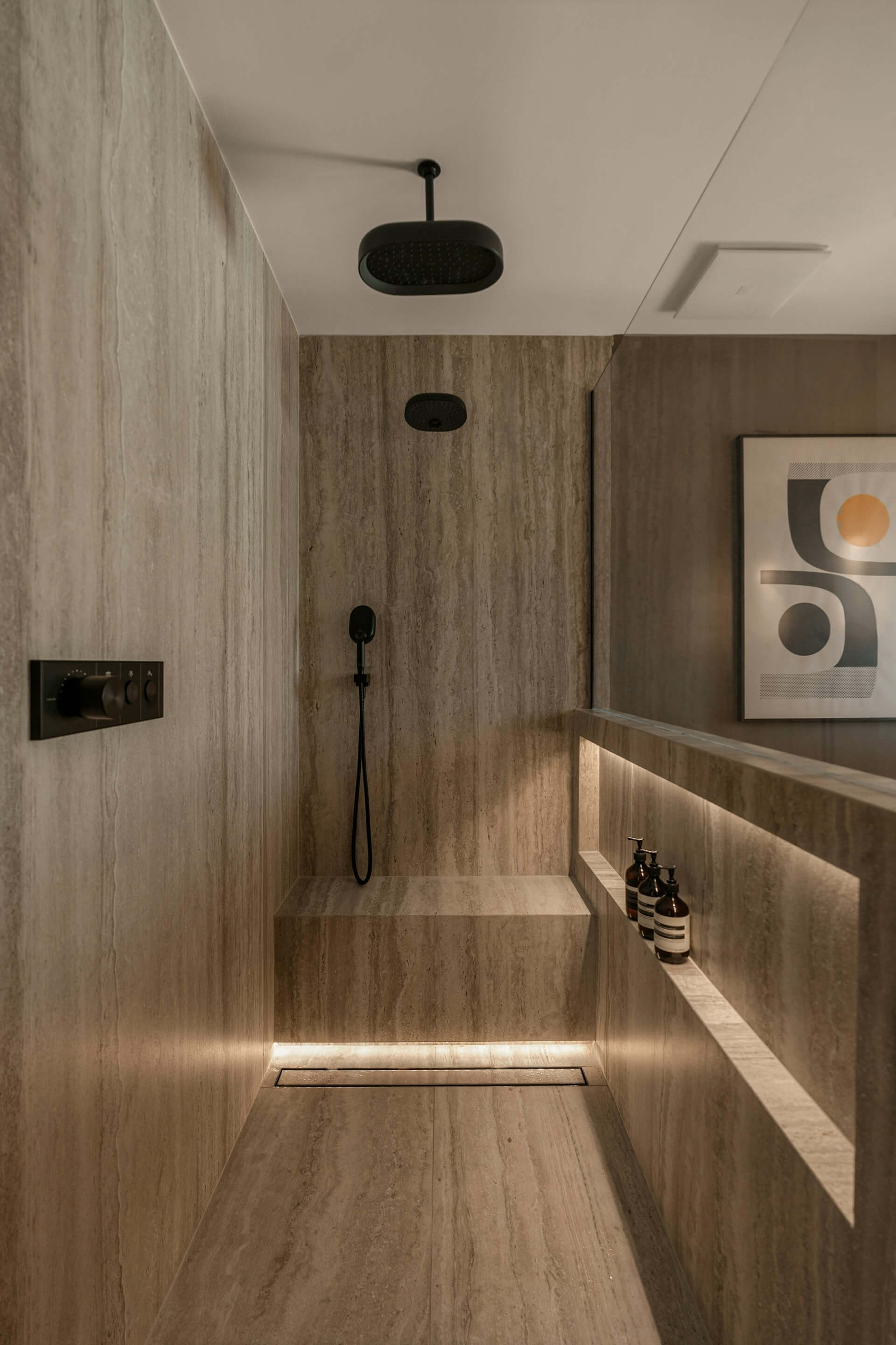 Minimalist walk-in shower with matte black fixtures, stone bench, and ambient niche lighting.