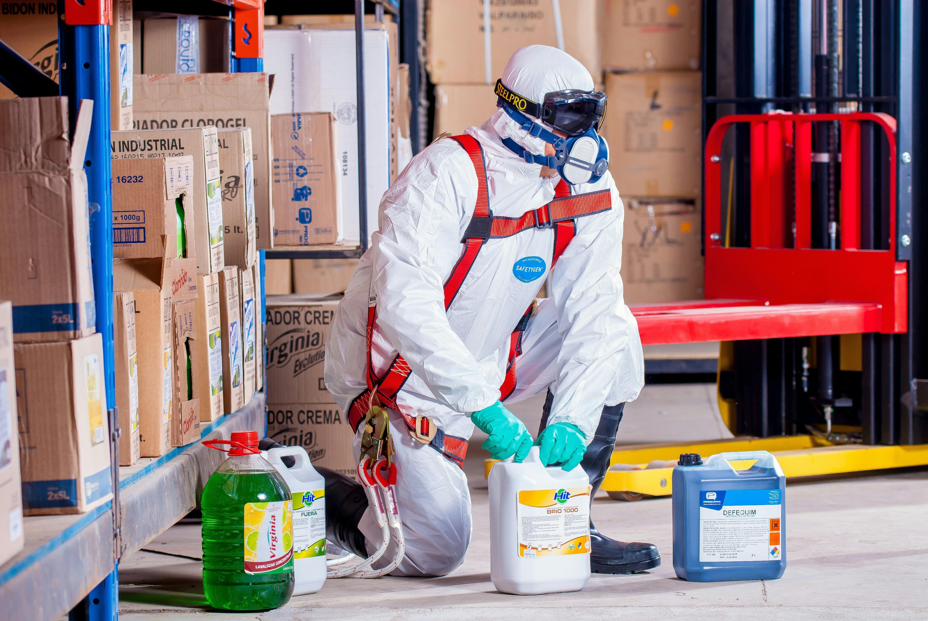 Professional cleaner in protective equipment handling cleaning chemicals and safety supplies in storage area