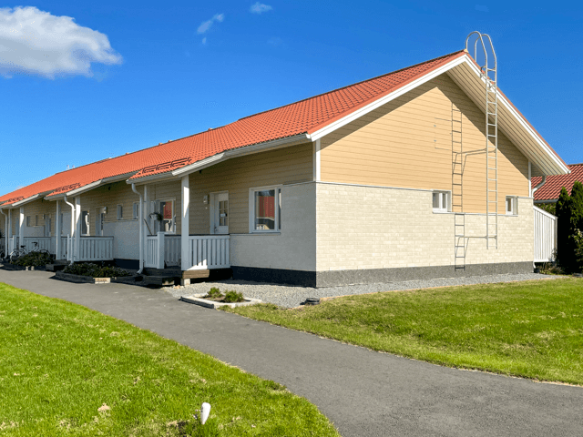 Ulkomaalattu vaalea rivitalo Nurmossa, punainen peltikatto ja siisti julkisivu, hyvin hoidettu nurmialue ja kävelytie