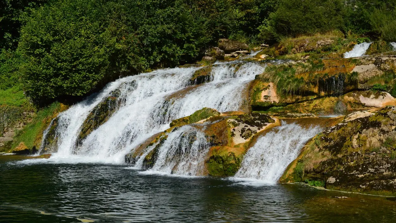 Waterfall surrounded by trees and grass in Bourg-de-Sirod, Bourgogne-Franche-Comté, France, ideal for eco-tourism, slow living, and green retreats.