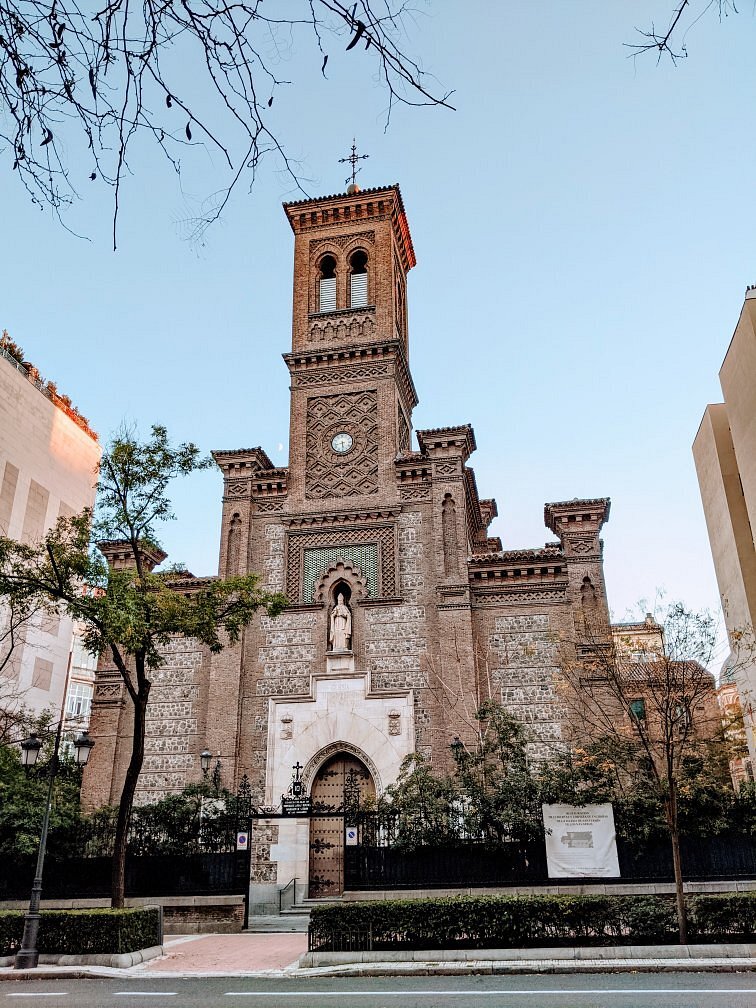 An elegant wedding ceremony setup features a domed gazebo adorned with peach and pink floral arrangements and lush greenery. White chairs line the aisle.