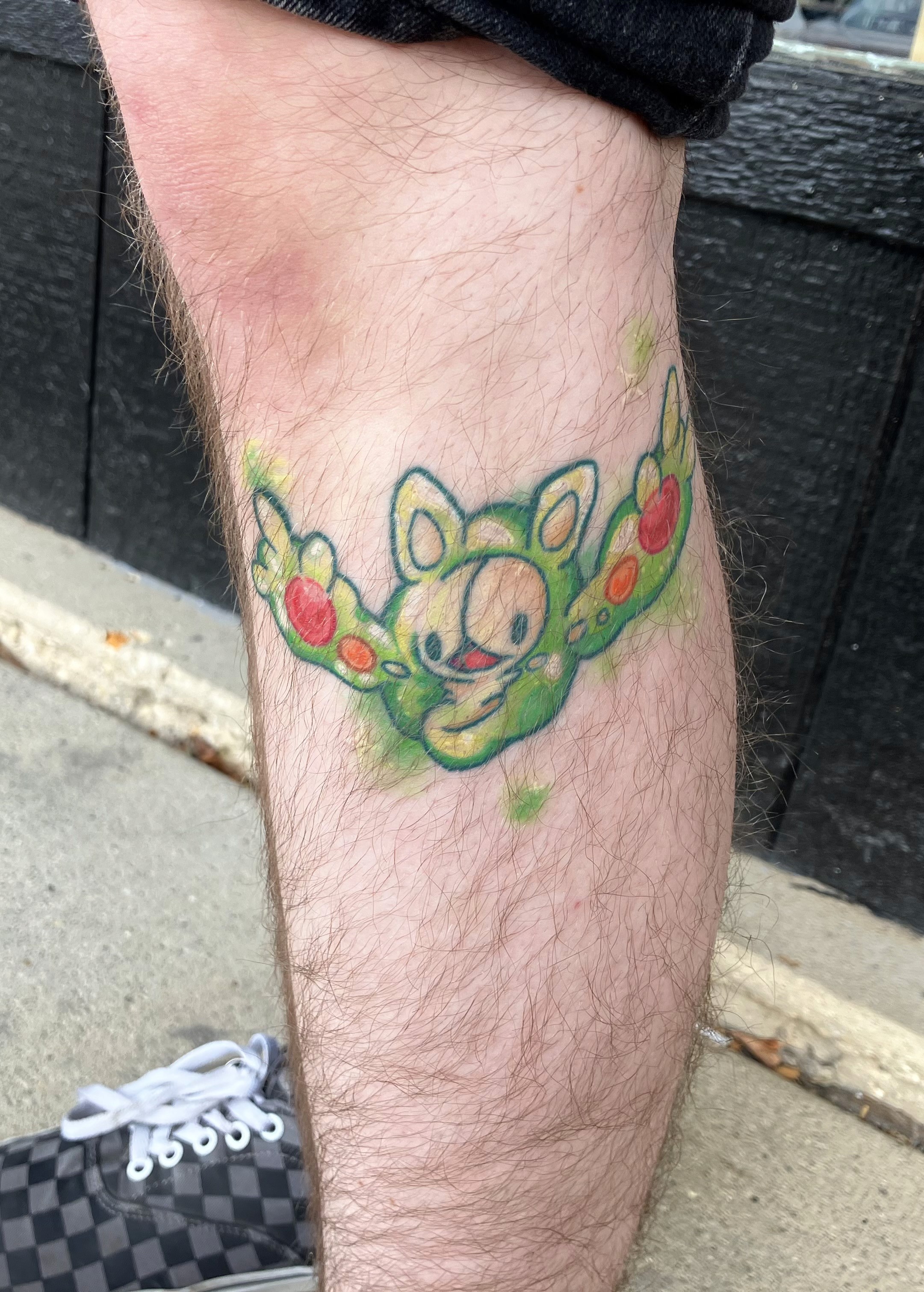 A vibrant tattoo of a chainsaw-like creature on a person's forearm. The tattoo is detailed with shades of orange, black, teal, and red.