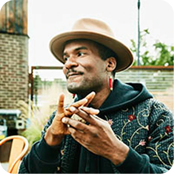 Creative professional wearing a stylish fedora hat and patterned hoodie looking aside in an outdoor setting.