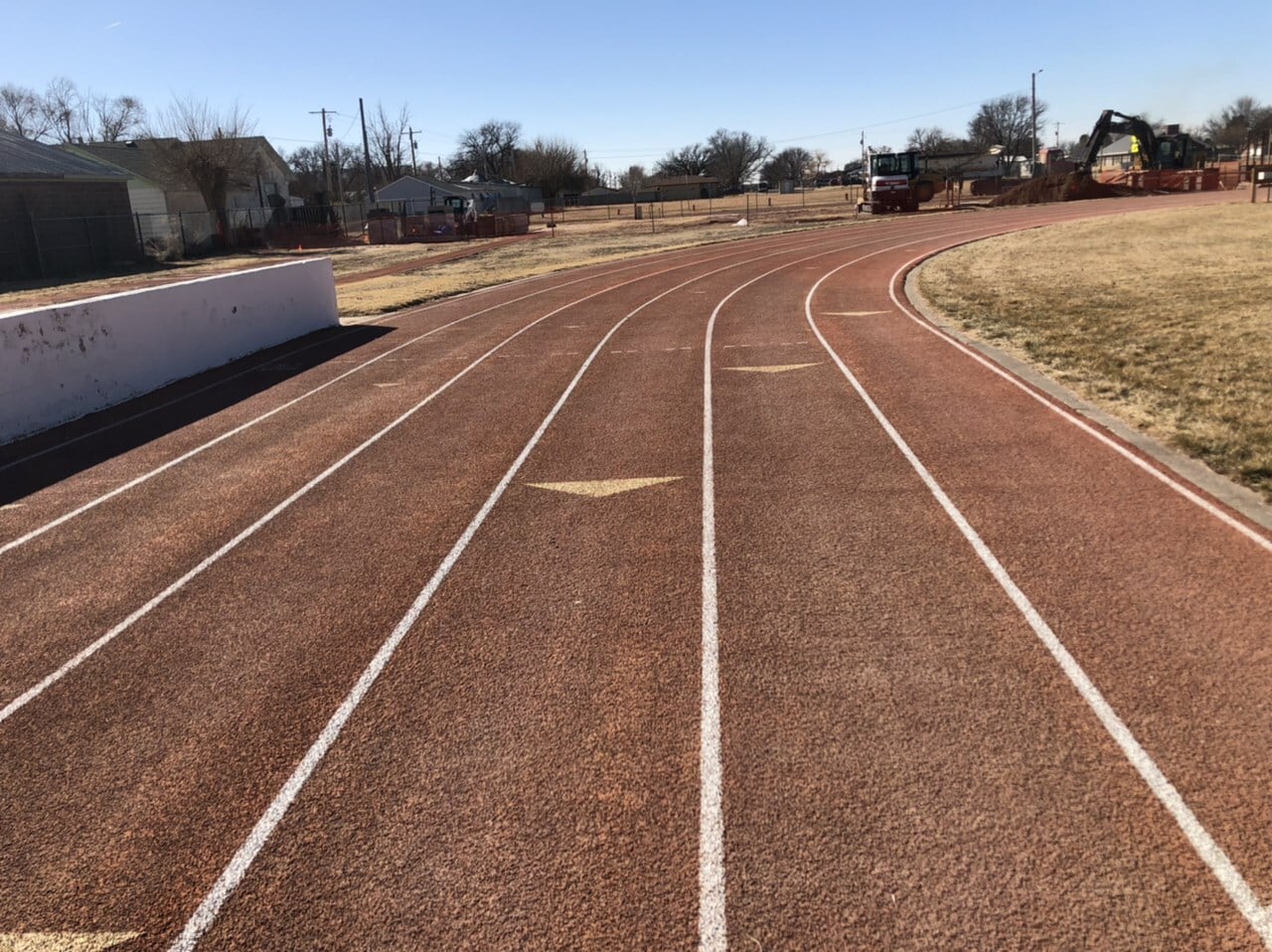 Faded red track curve with equipment behind before resurfacing at Ulysses High School in Ulysses, KS