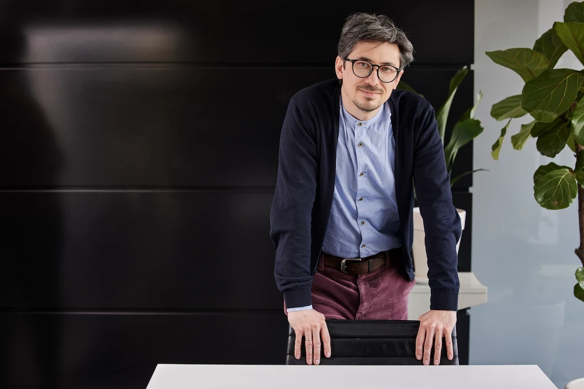Person steht an einem Tisch in einem modernen Büro mit dunkler Wand und Pflanze im Hintergrund