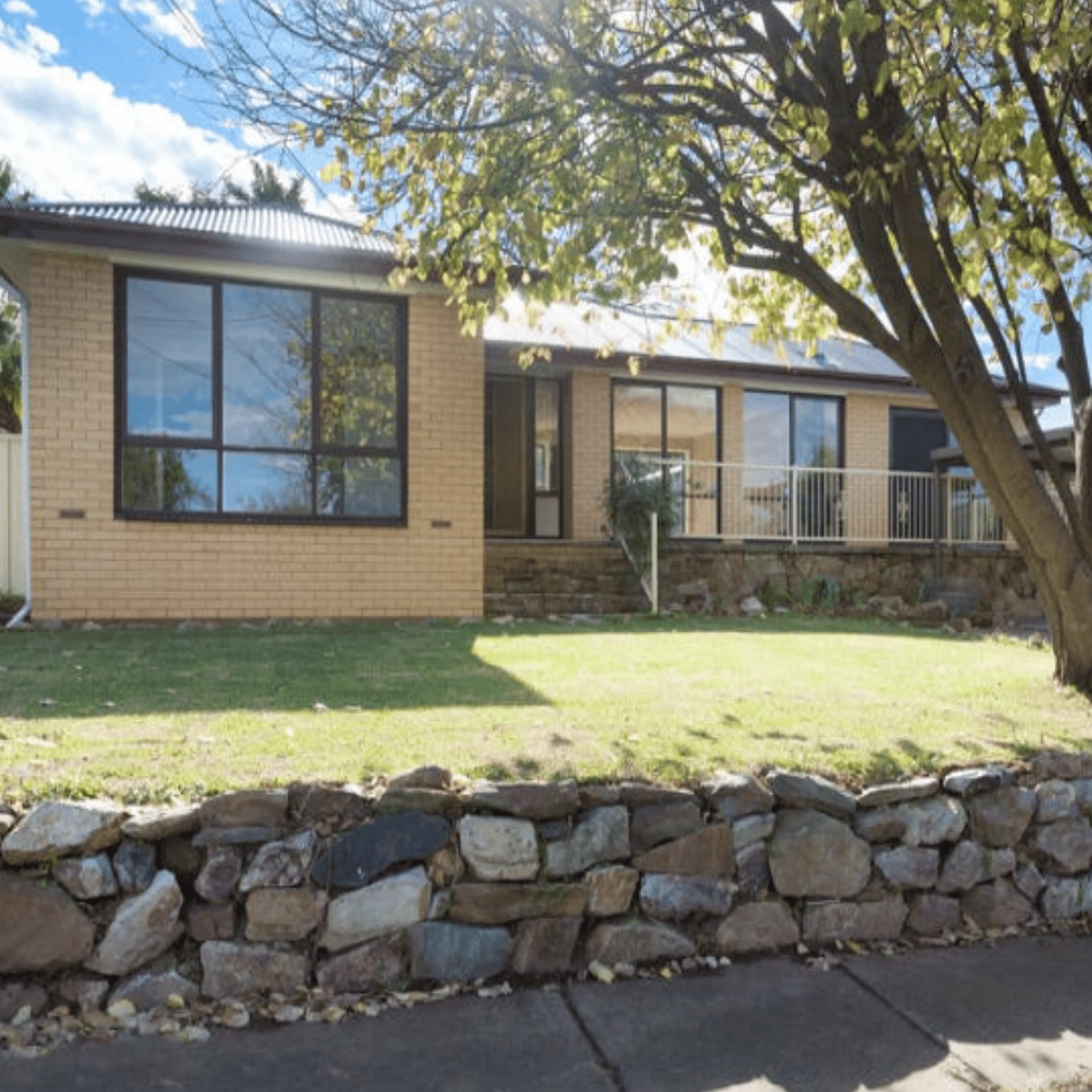 Brick house with large windows and a stone wall.
