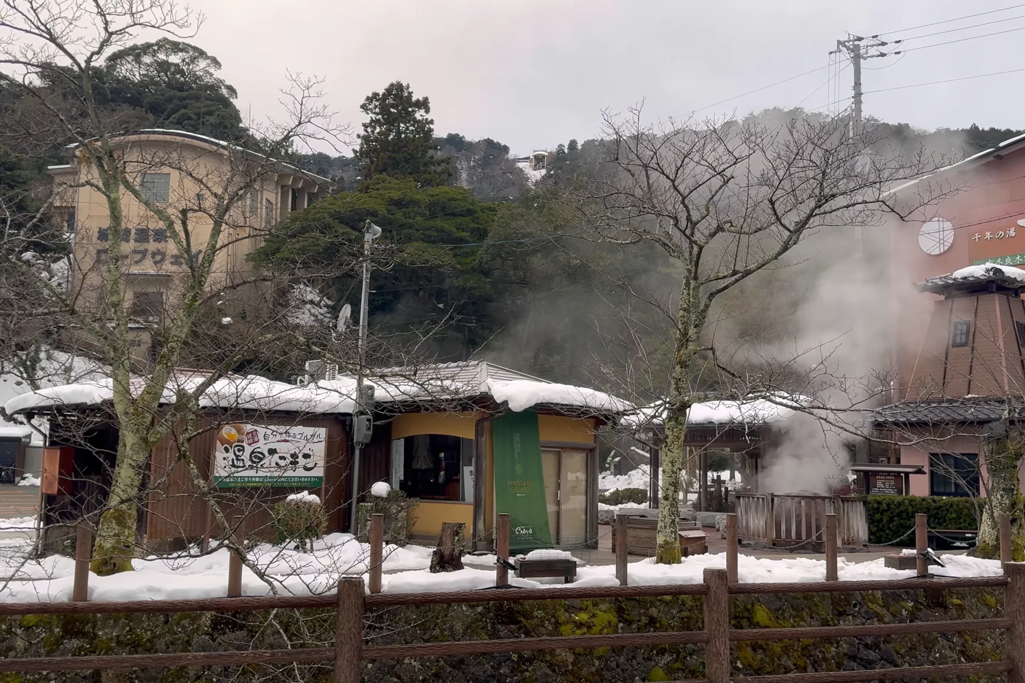 Steam billowing from the Kinosaki hot spring source across a snow-covered garden and fence.