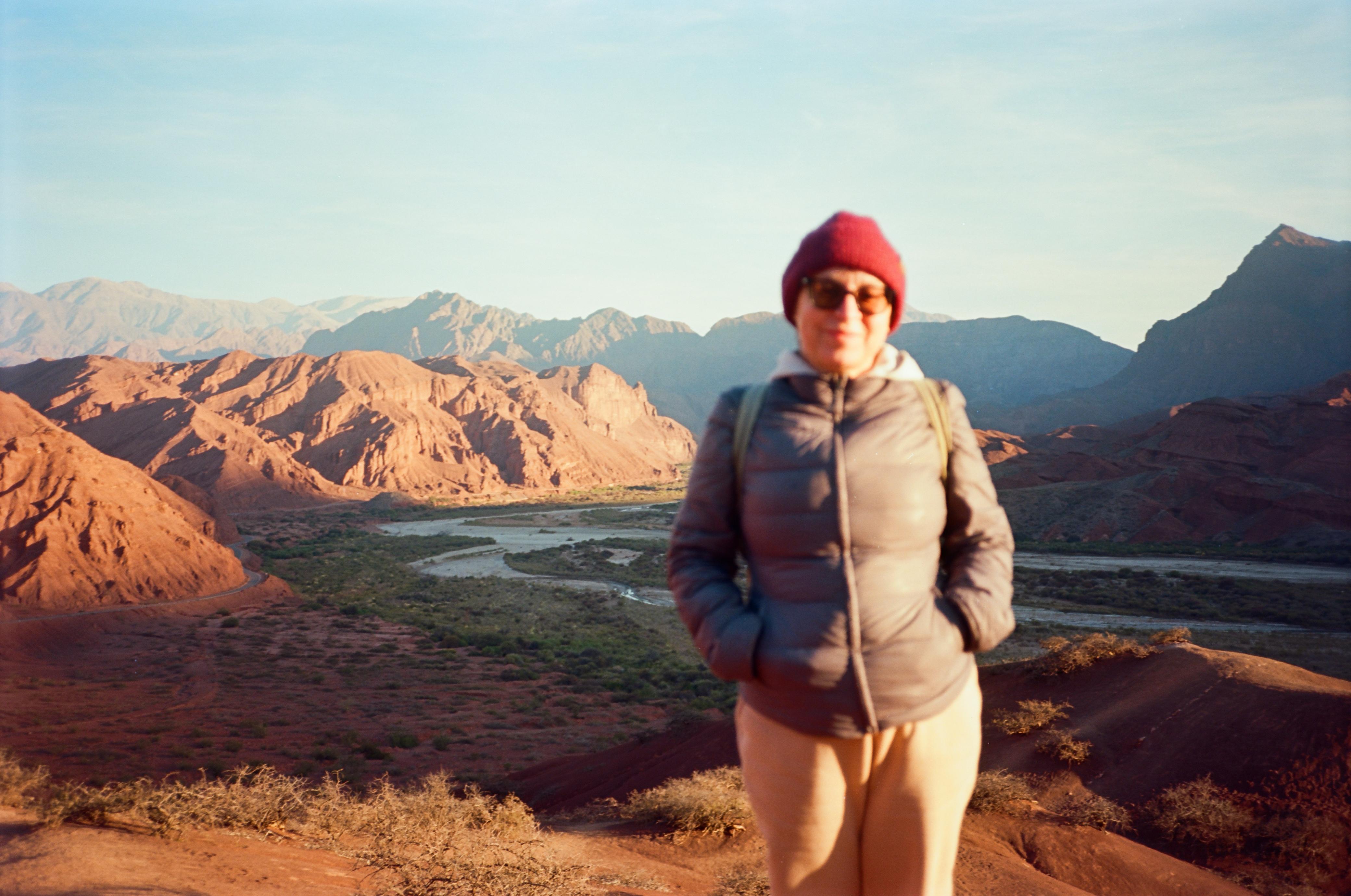 Mujer sentada sobre un tronco frente a una cascada doble en un bosque frondoso de Argentina.