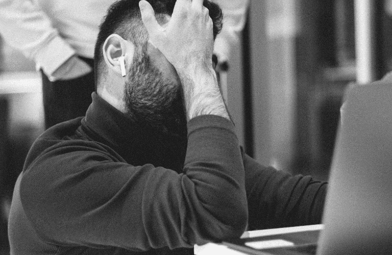 Gestresste bedrijfseigenaar houdt zijn hoofd vast terwijl hij naar een laptop kijkt