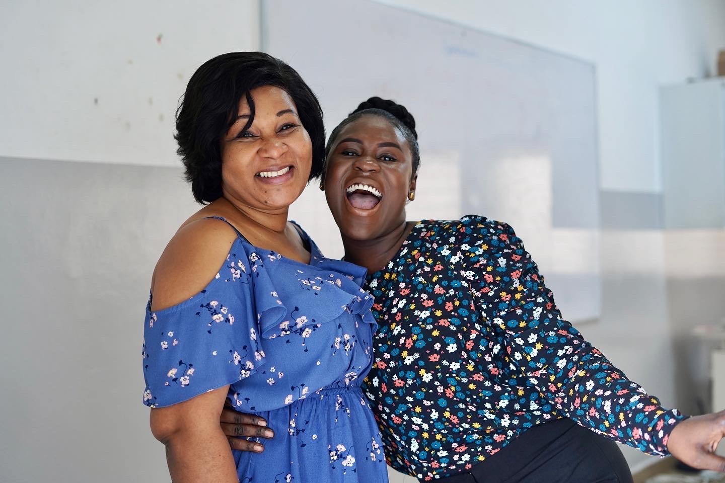 A smiling student in a white shirt and tie sits at a desk in a colorful classroom, engaged in learning.
