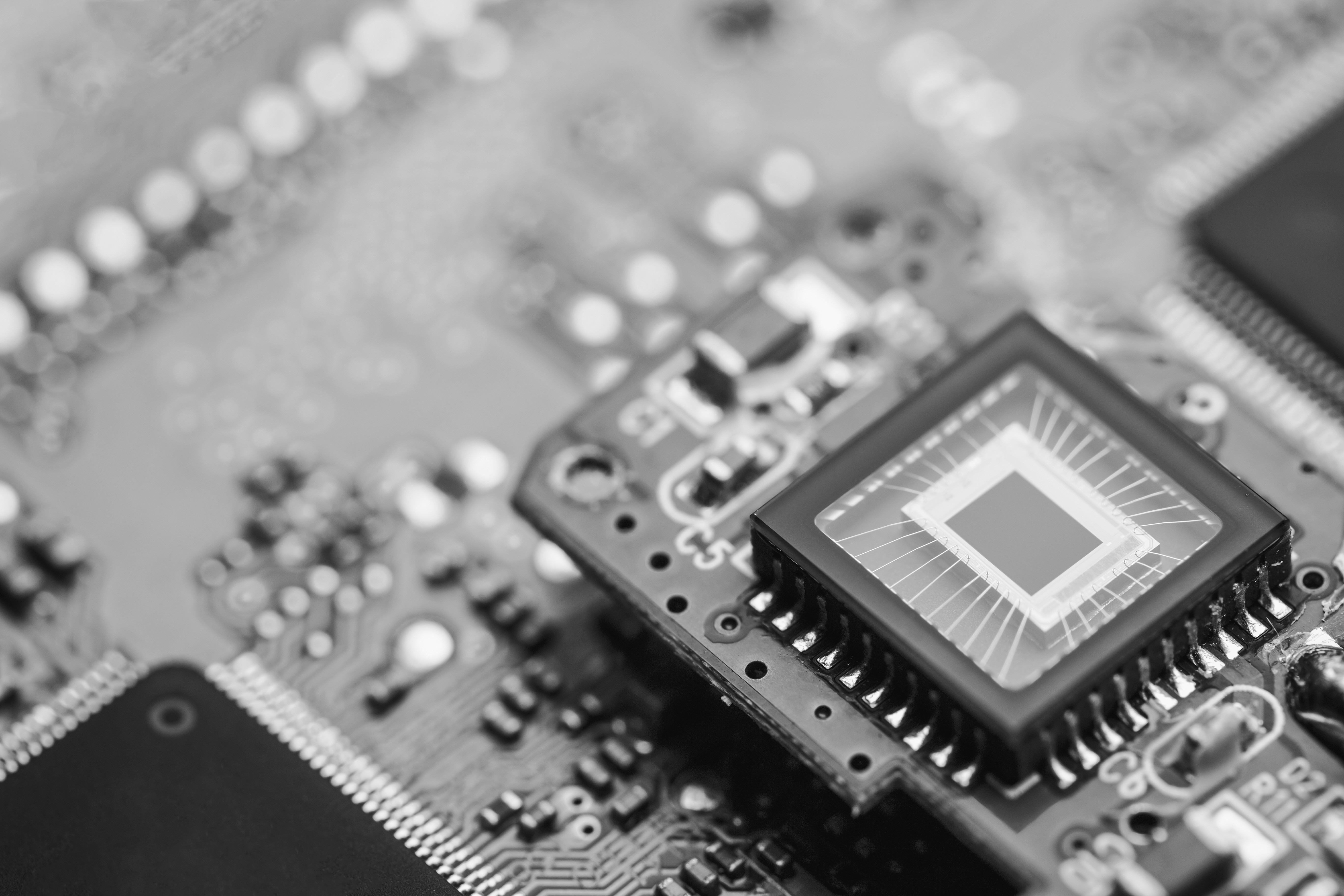 Close-up of a computer chip on a circuit board, showcasing intricate patterns and connections in black and white.