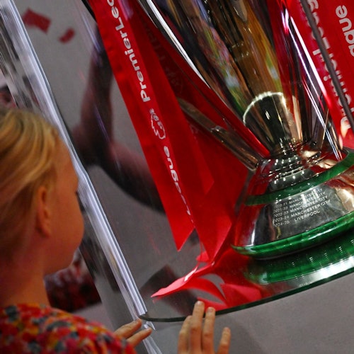 ילד מתבונן בגביע הפרמייר ליג עם סרטים אדומים מבעד לוויטרינת זכוכית.