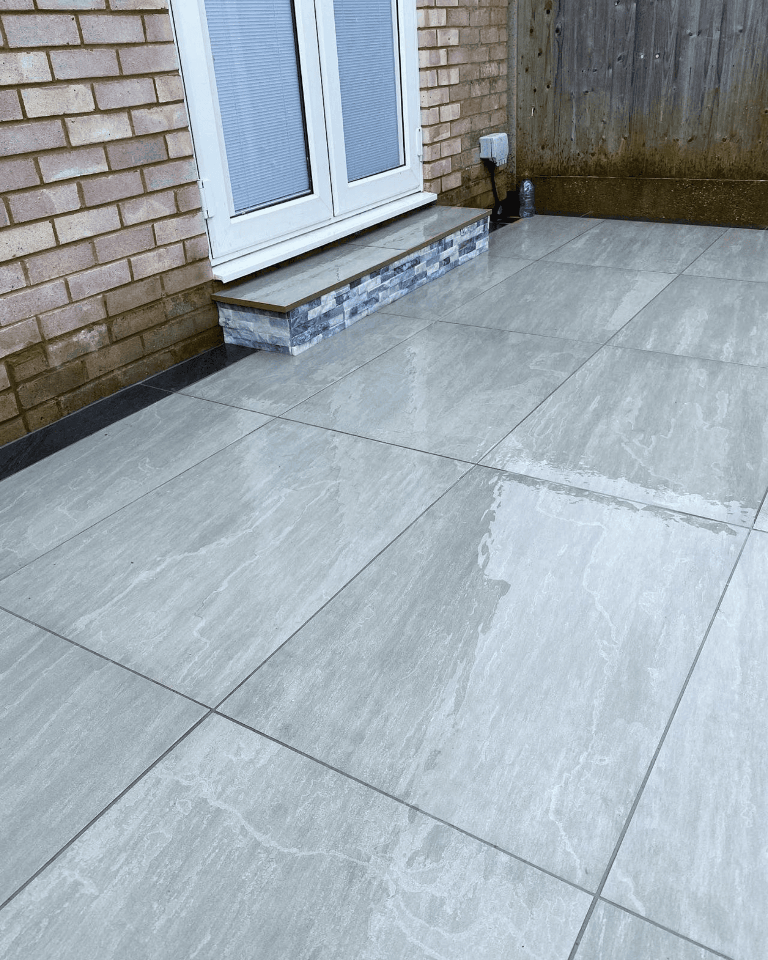 Close-up of new grey porcelain patio tiles and a custom tiled step at the back door, installed by PPM Builders in Northampton for a contemporary outdoor space.