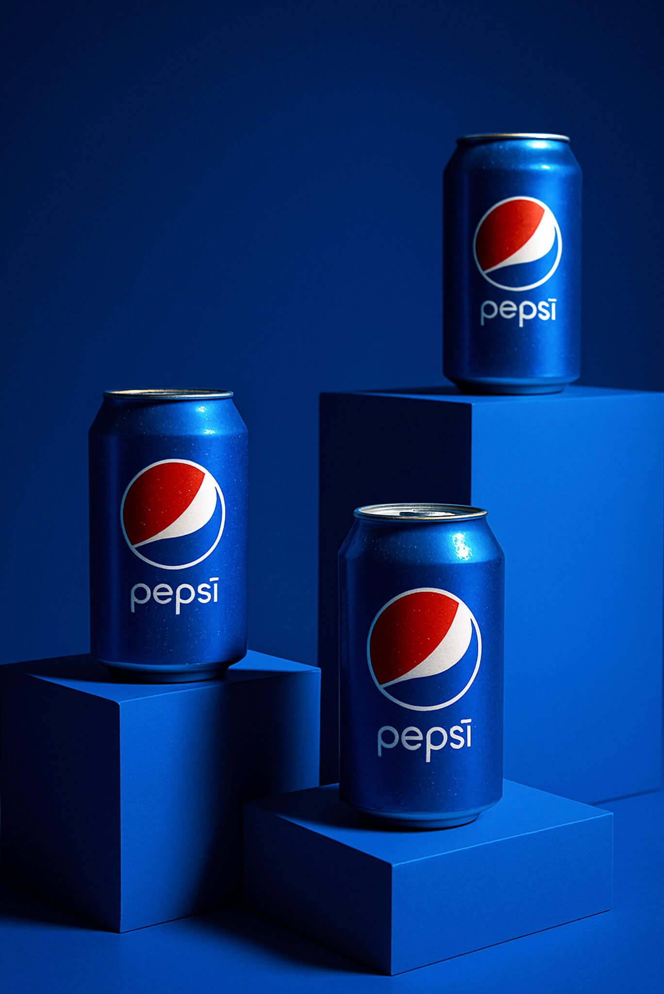 Three Pepsi cans displayed on blue geometric platforms with a matching blue background, showcasing brand identity.