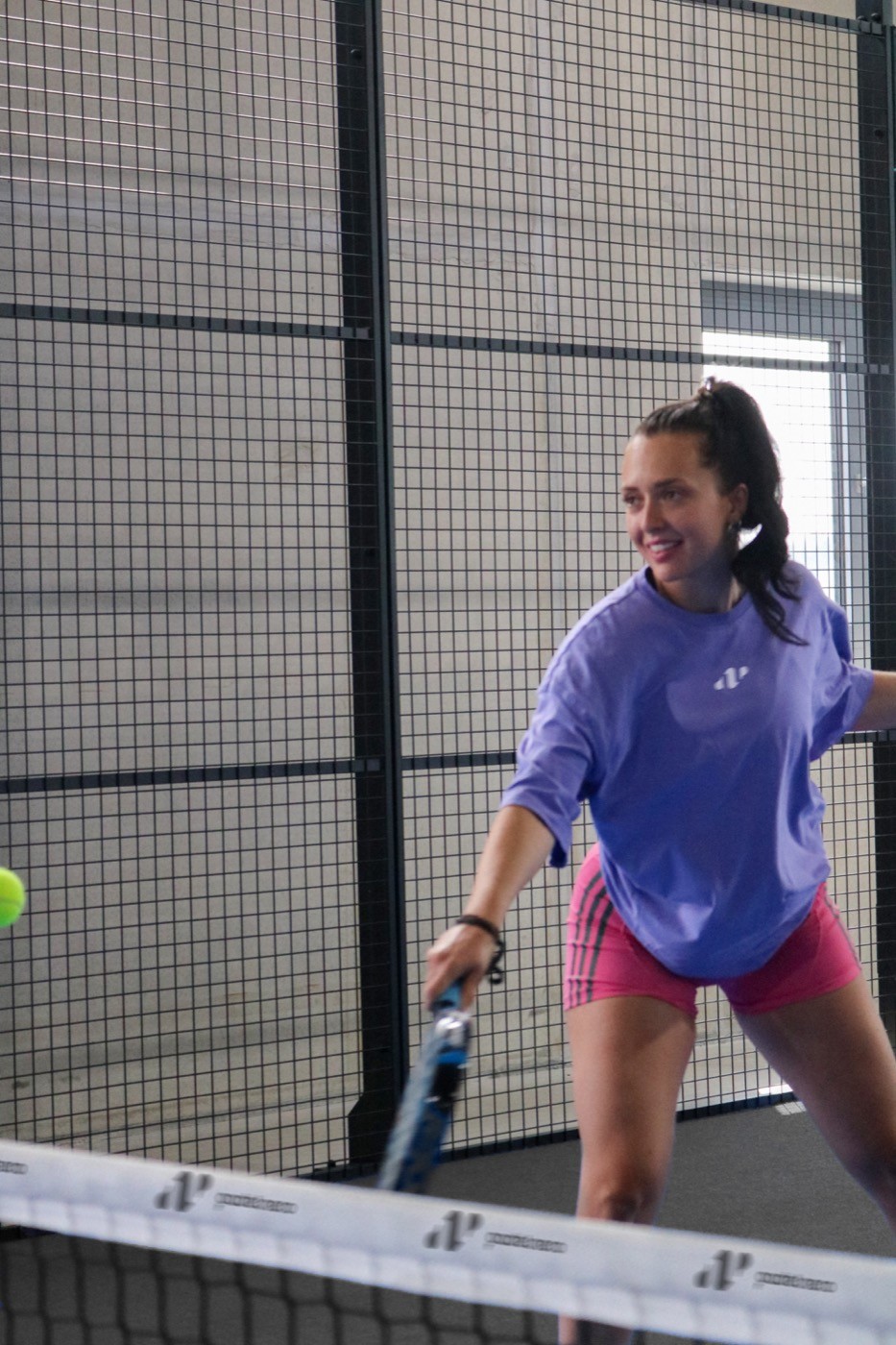Padelspielerin im lilafarbenen Shirt und pinken Shorts konzentriert im Spiel – Freude und Energie auf dem Padelnero Court.