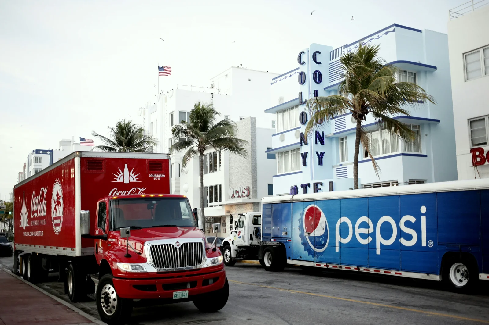Coca-Cola and Pepsi delivery trucks parked outside the Colony Hotel in Miami Beach, showcasing competing beverage brand loyalty programs.