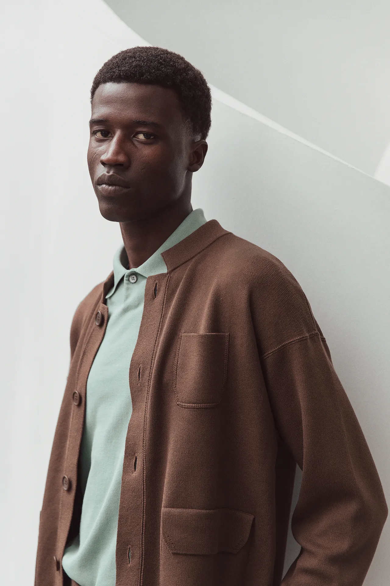 Close-up of Aida Barni SS26 collection men's brown knit cardigan featuring patch pockets, worn over a mint green polo shirt.