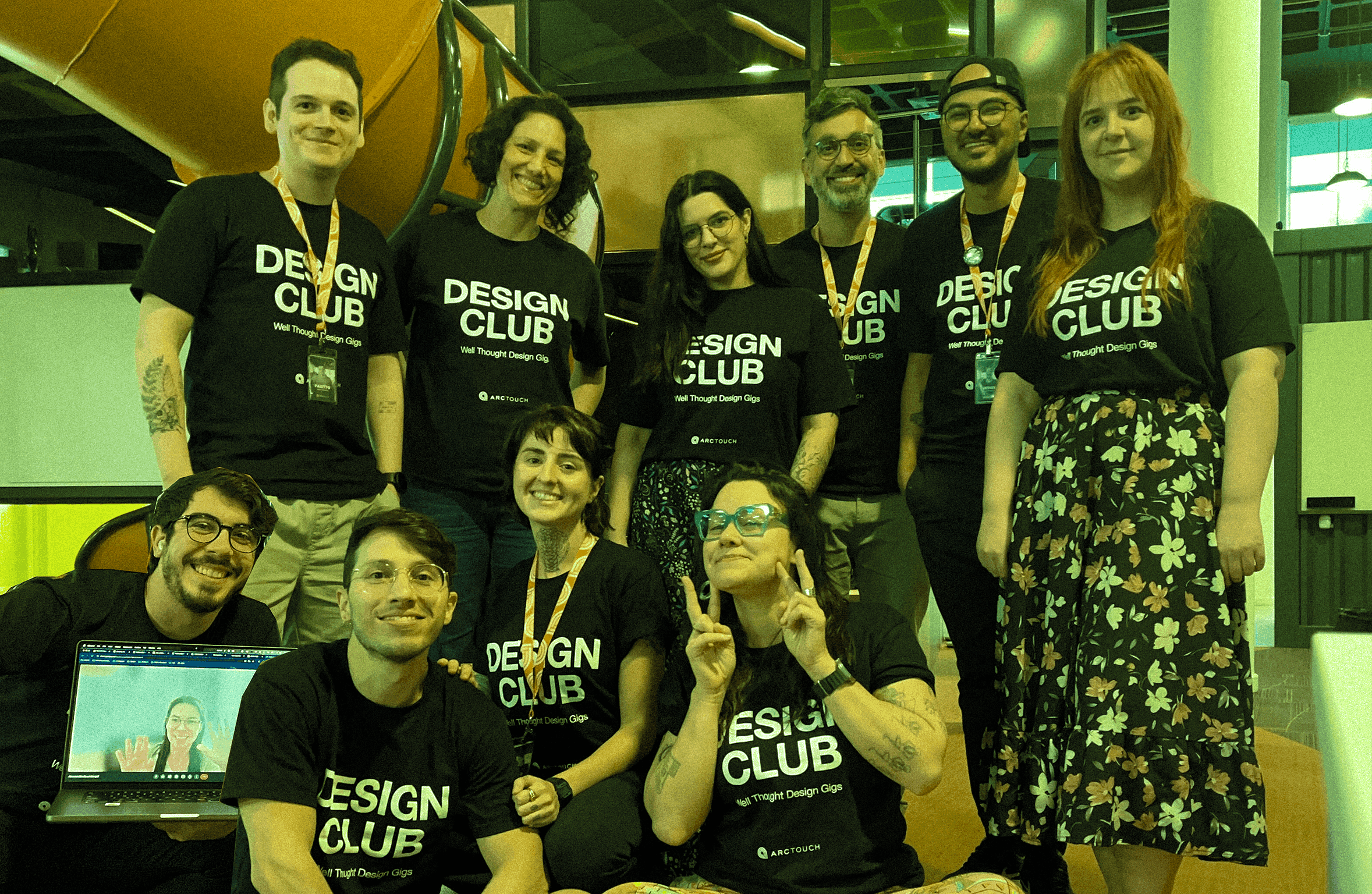 A diverse group of team members smiling together, wearing matching black t-shirts with 'Design Club' printed on them.