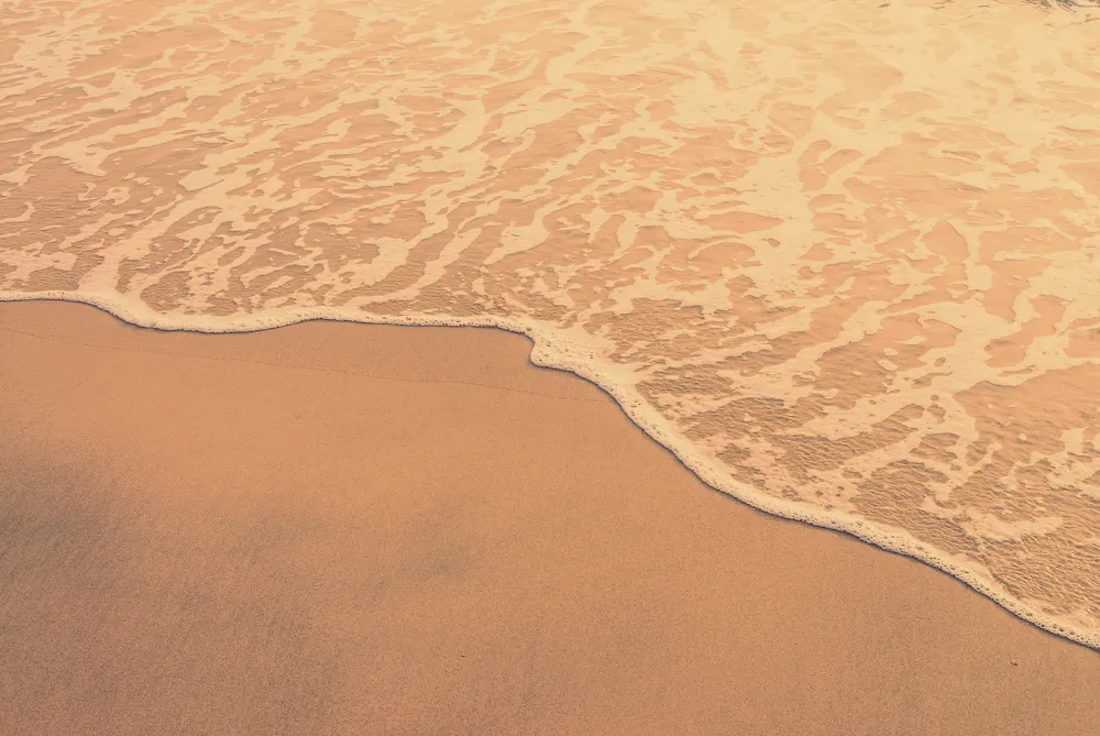 Ondas do mar encontrando a areia representando a equipe e o cuidado em cada detalhe