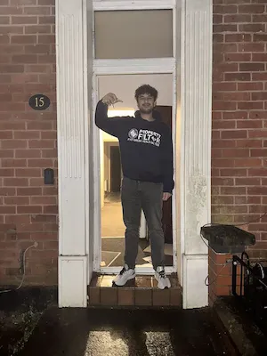 Person standing in the doorway of a brick house holding what appears to be keys