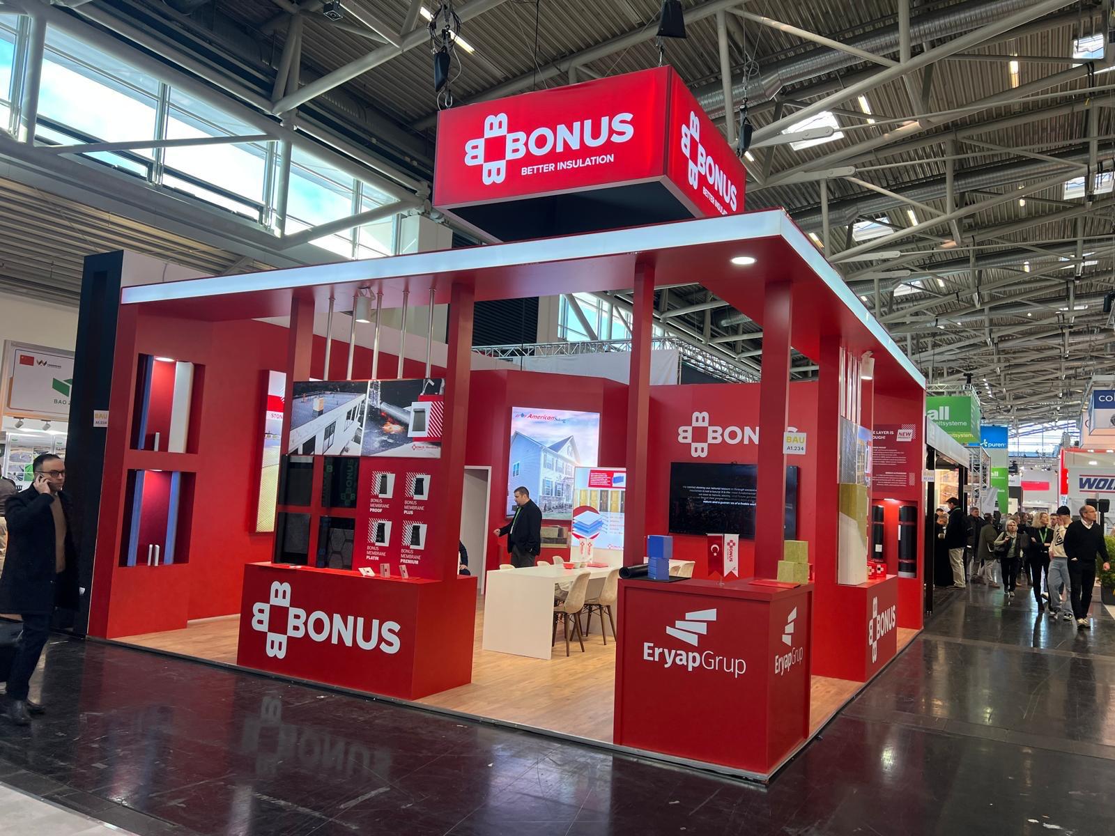 BONUS exhibition stand at BAU 2025 Munich, featuring a bold red corporate identity, large red architectural frames, and strong illuminated branding.