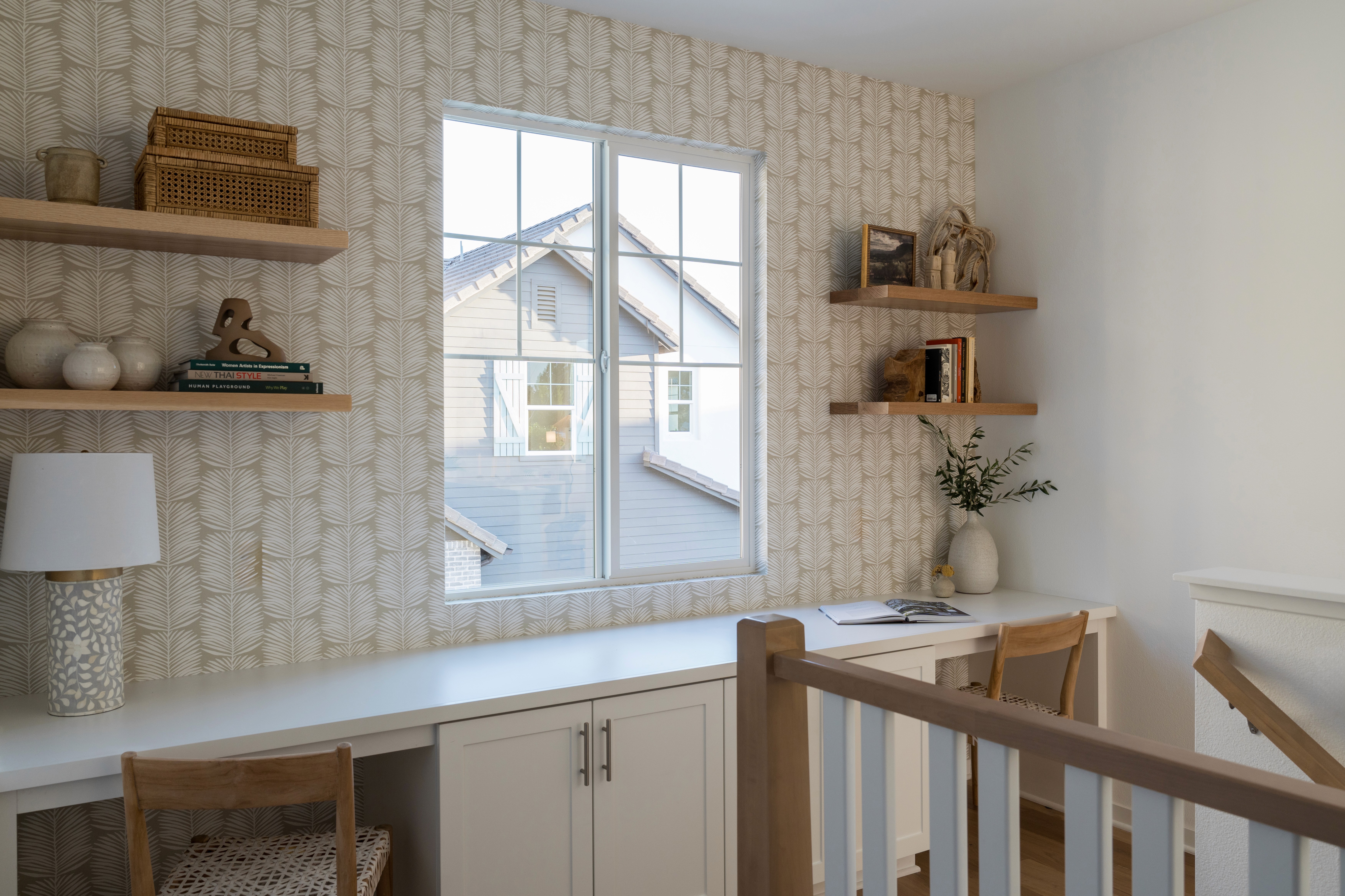 Stair landing with wall to wall desk space, wood desk chairs, open wood shelving, and patterned wall paper by Jubilee Interiors in Arcadia, California