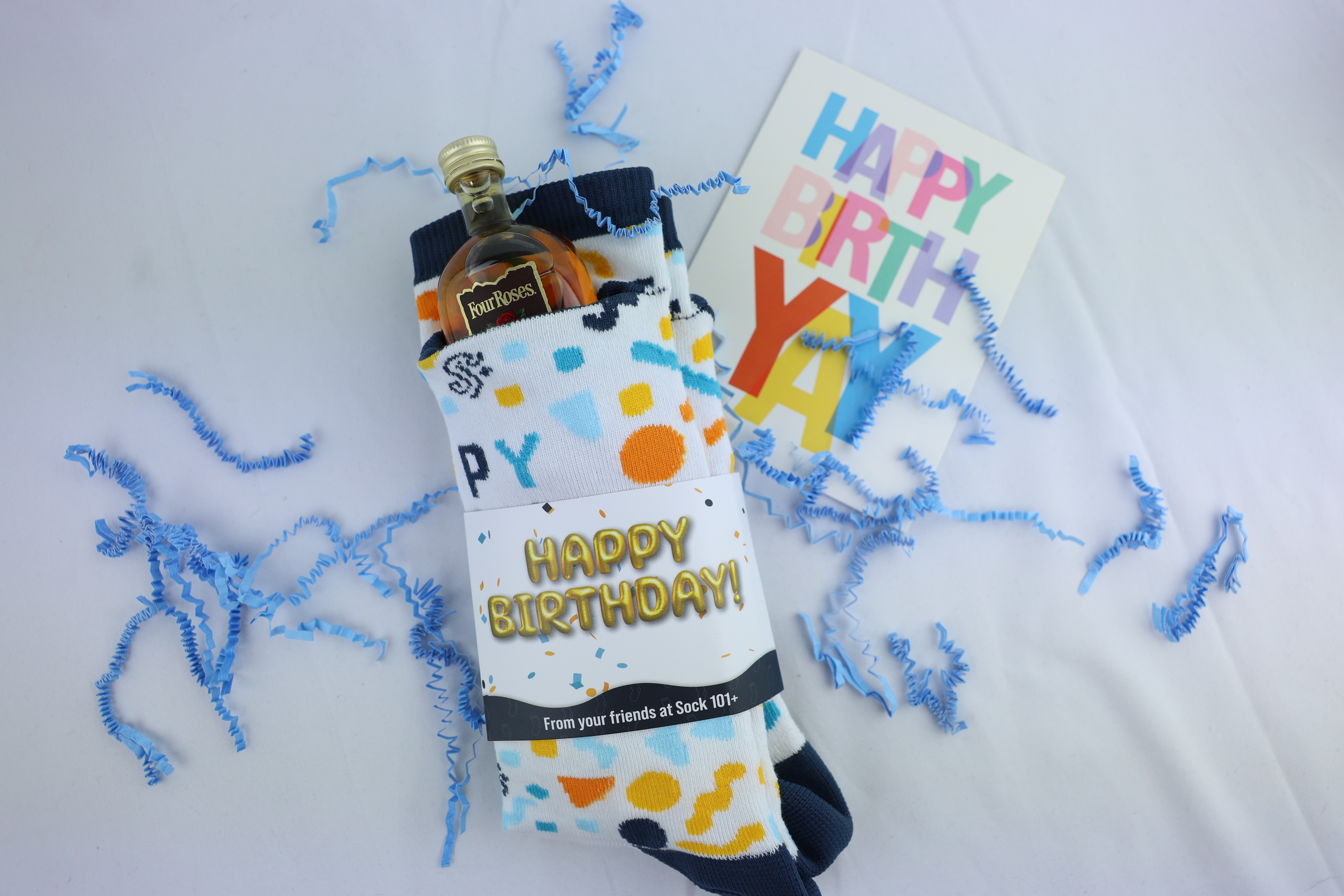 Stash socks holding a shooter bottle. The socks say happy birthday and there is a card on the right hand side.