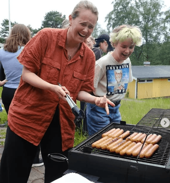 A person smiling while grilling hot dogs.