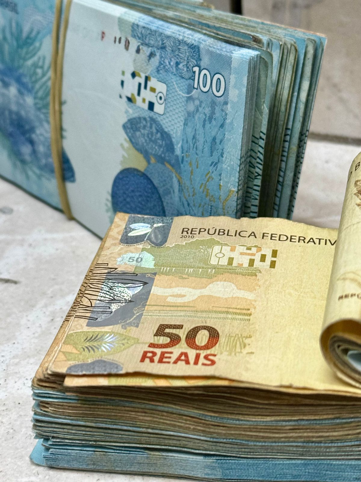 Notas de real brasileiro de 50 e 100 empilhadas, representando a comissão e a remuneração variável de vendas.