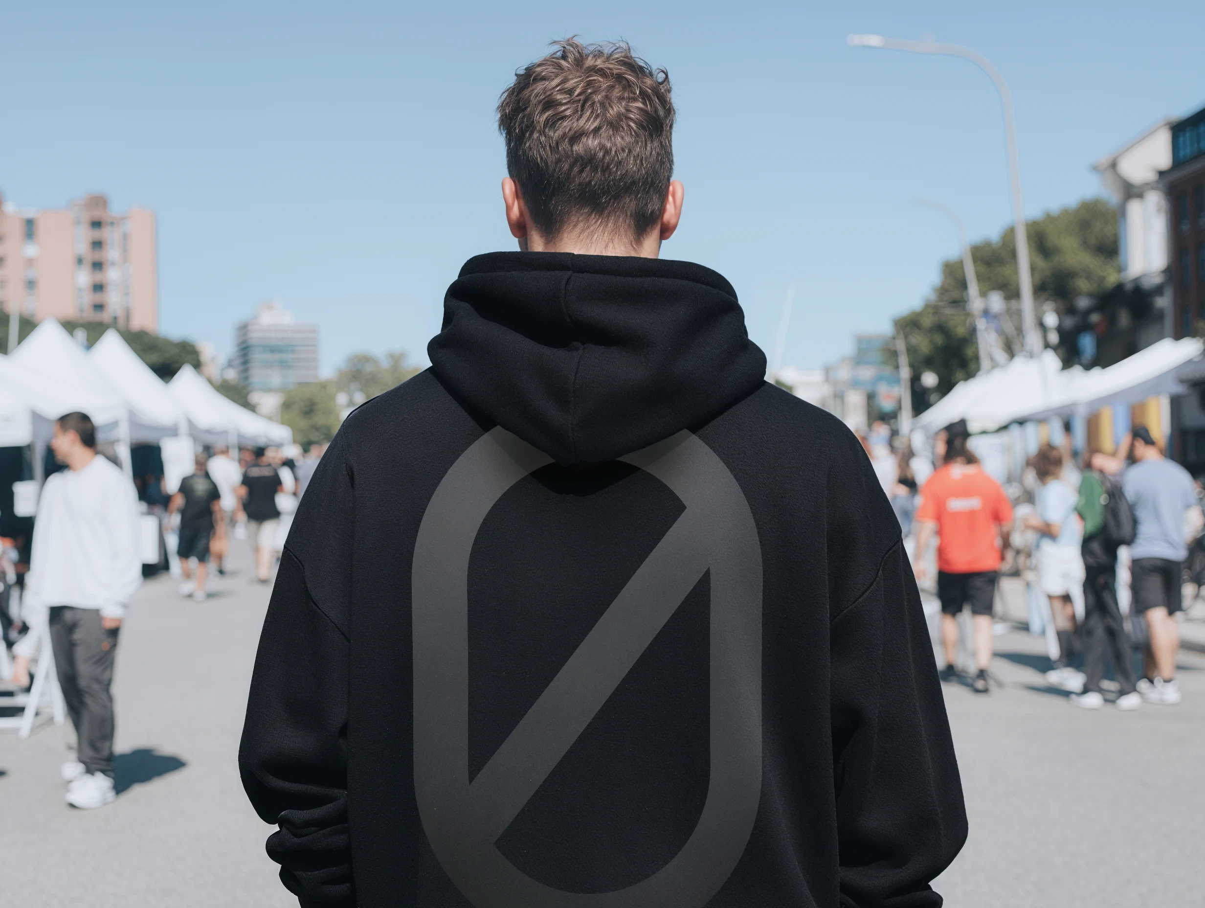 Back view of a person wearing a black hoodie with a graphic print in an outdoor market setting