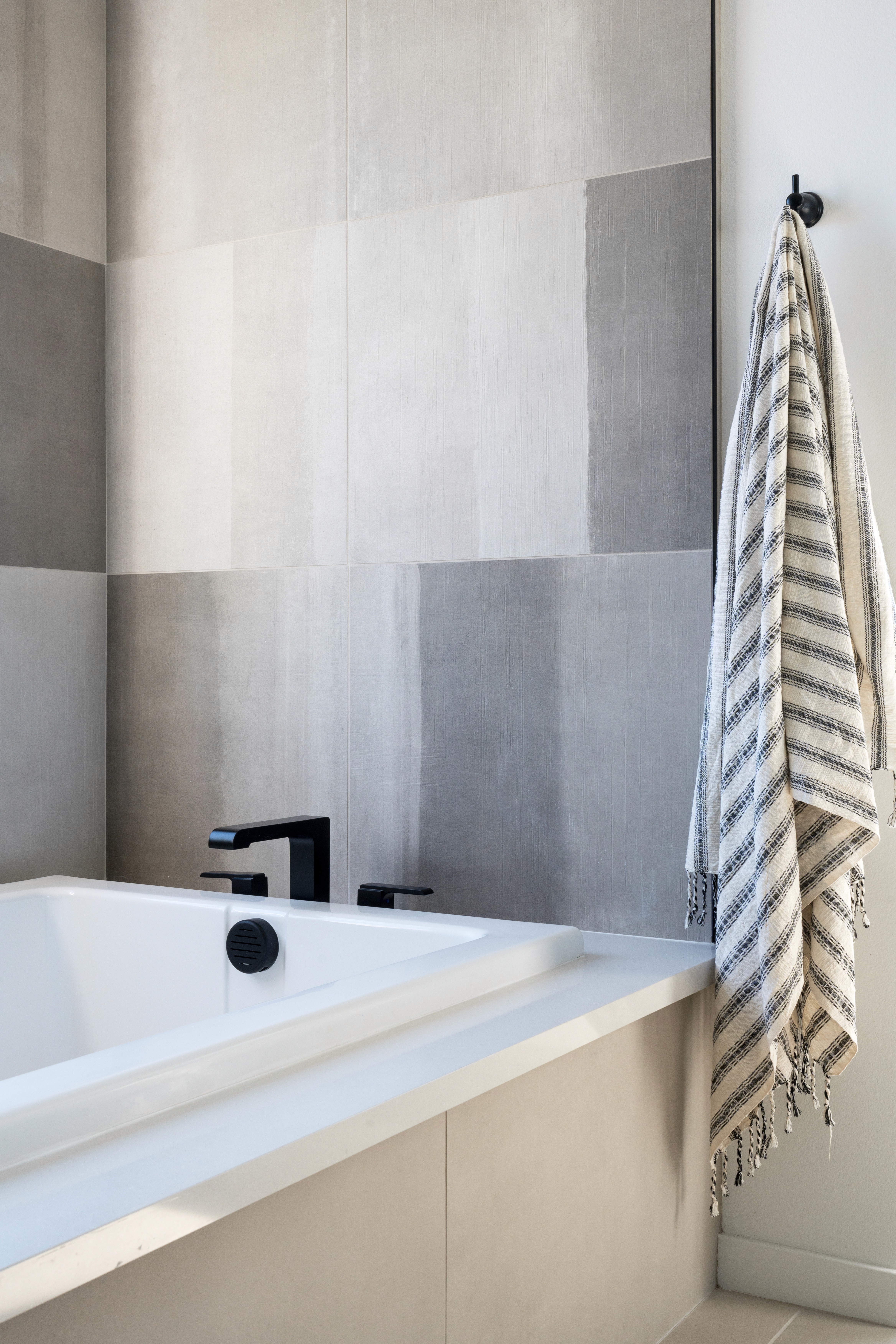 White, rectangular bathtub with black faucet and grey and white tiled wall by Jubilee Interiors in Arcadia, California