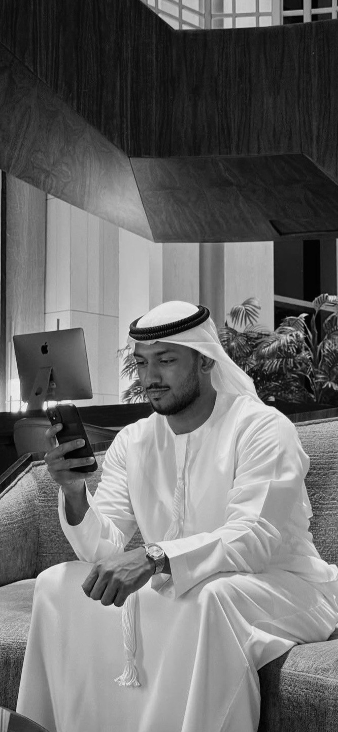 An ostrich is peeking at a man who is reading a newspaper.