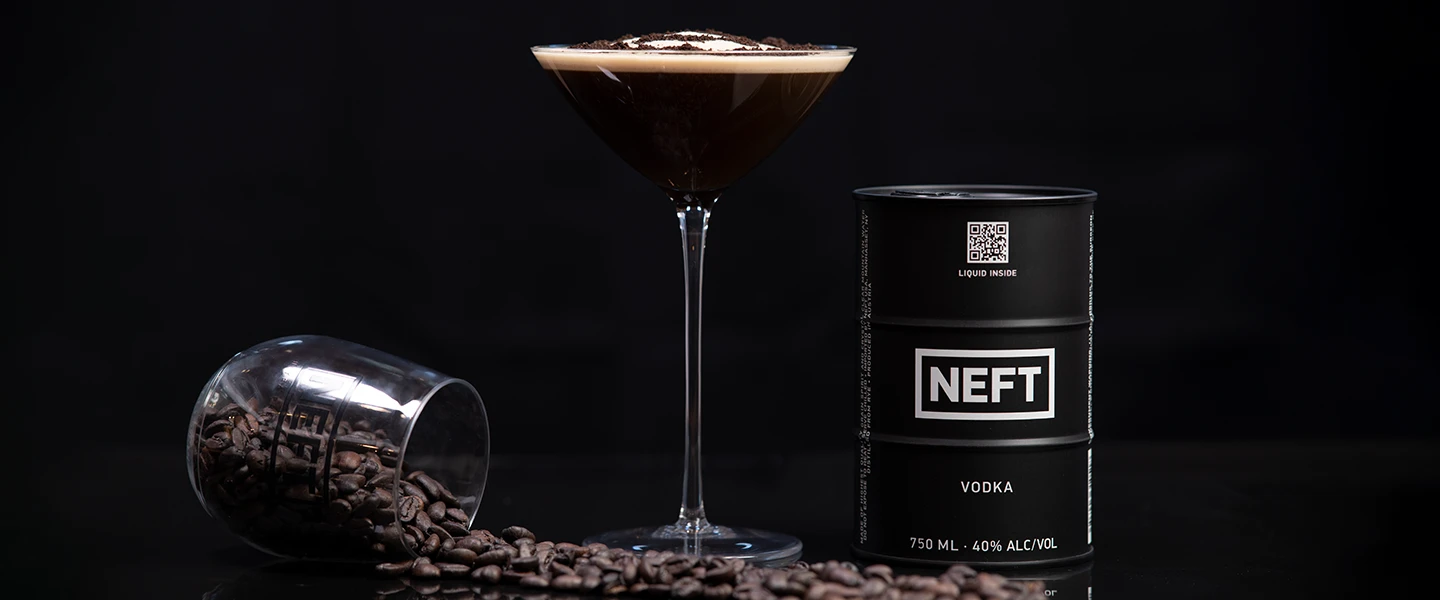 An espresso martini with a NEFT Vodka barrel and coffee beans against a dark background.