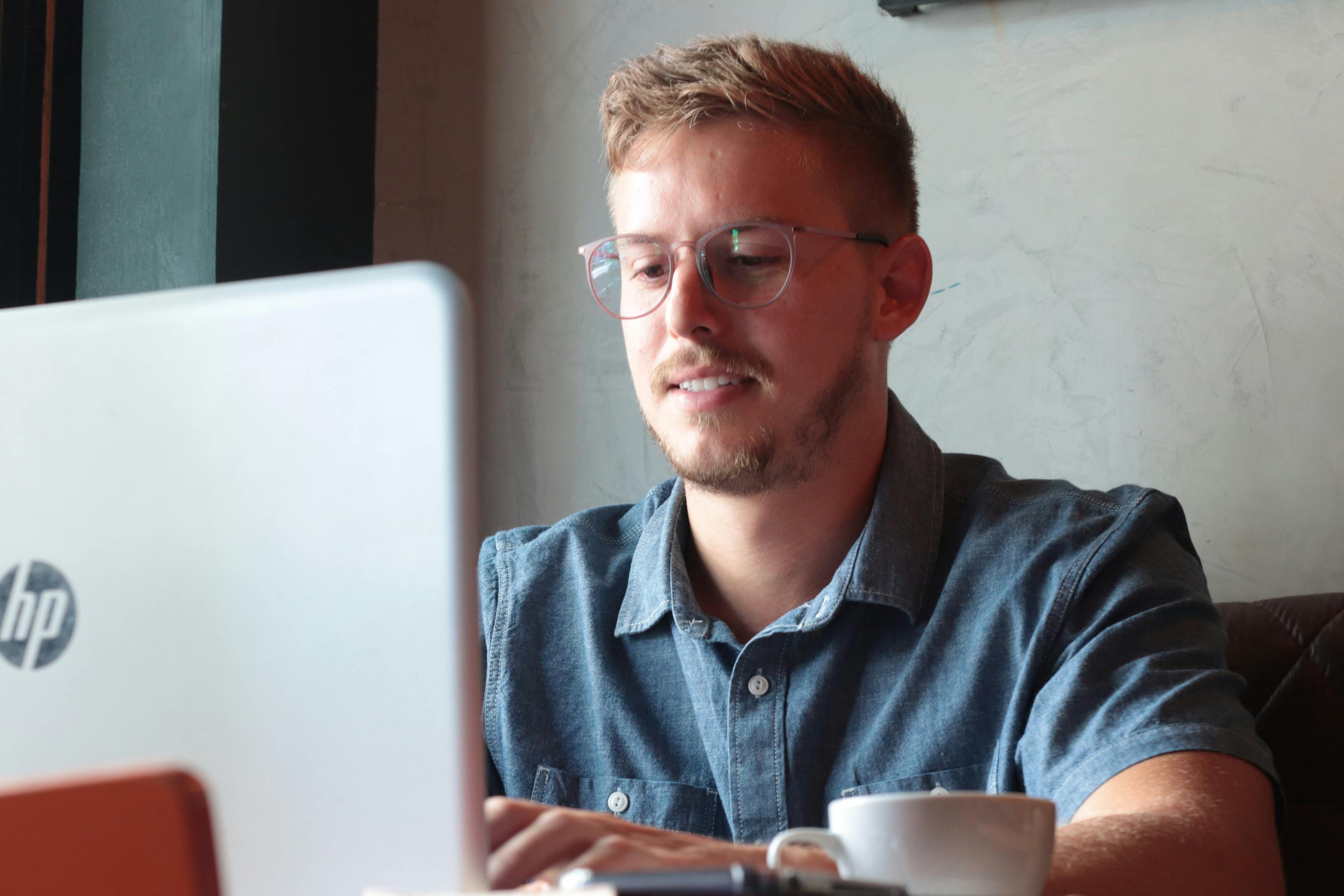 Front view of a man working on a laptop with a coffee next to them