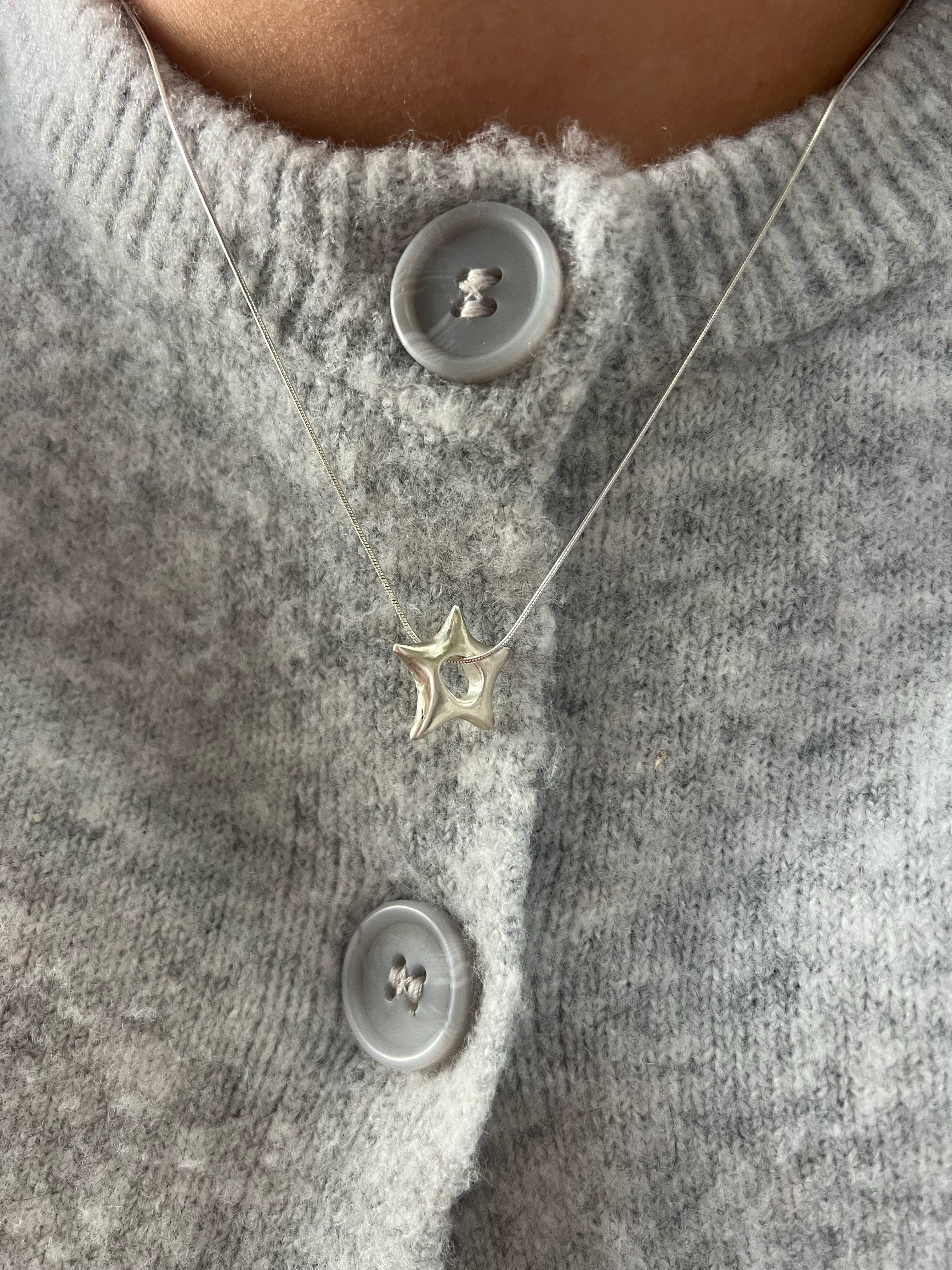 Silver star-shaped necklace on a gray textured fabric background