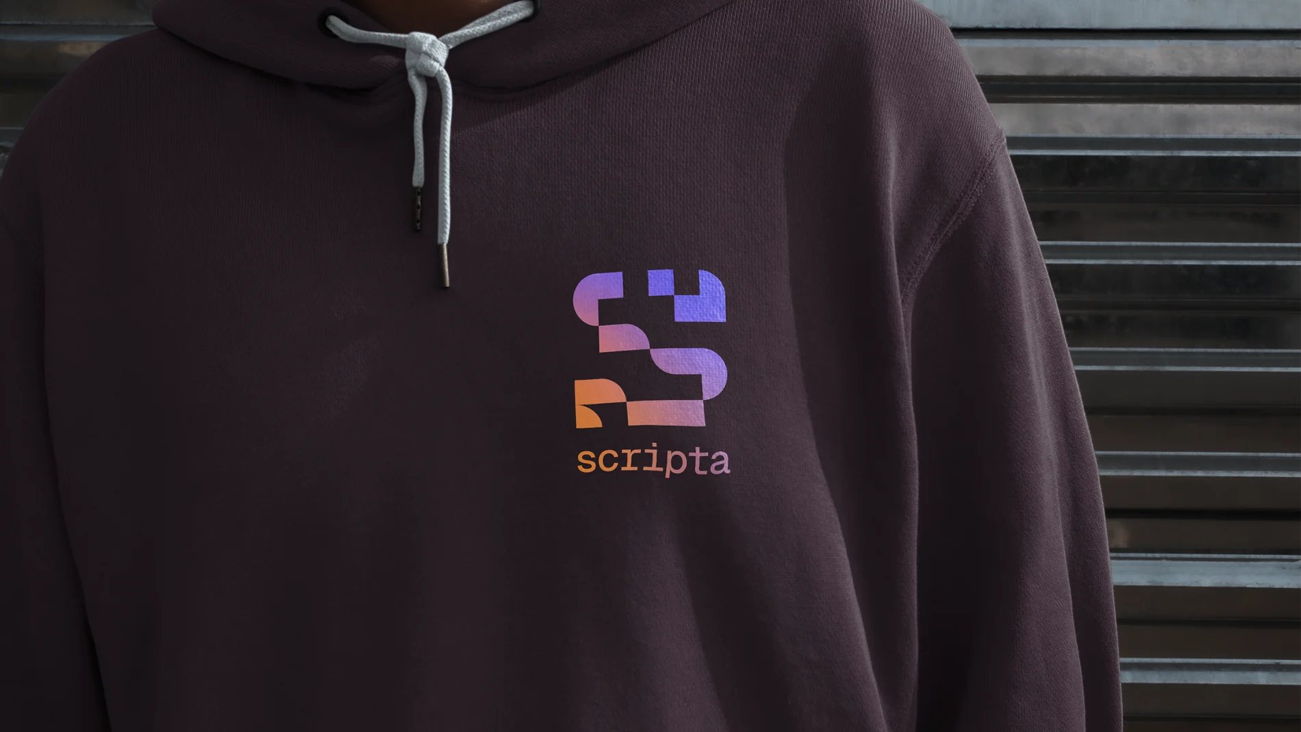 Close-up of a person wearing a dark hoodie with the Scripta logo and name in a gradient of purple and orange on the chest.