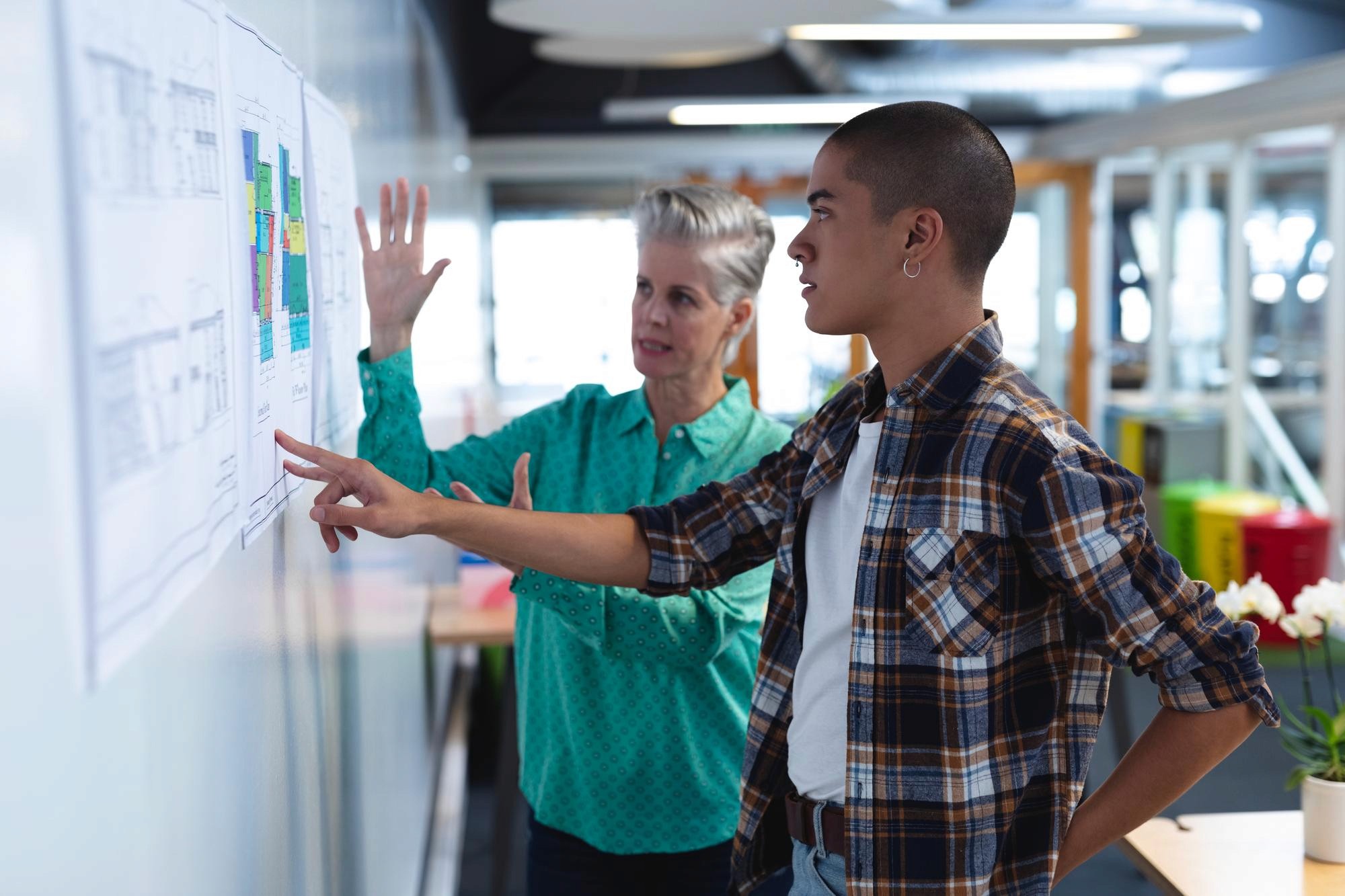 Two colleagues reviewing plans on a wall in a modern office, discussing layout and next steps.