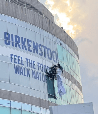 ช่างติดตั้งมีใบ จป. กำลังติดตั้งงานพิมพ์ mesh โฆษณา Birkenstock