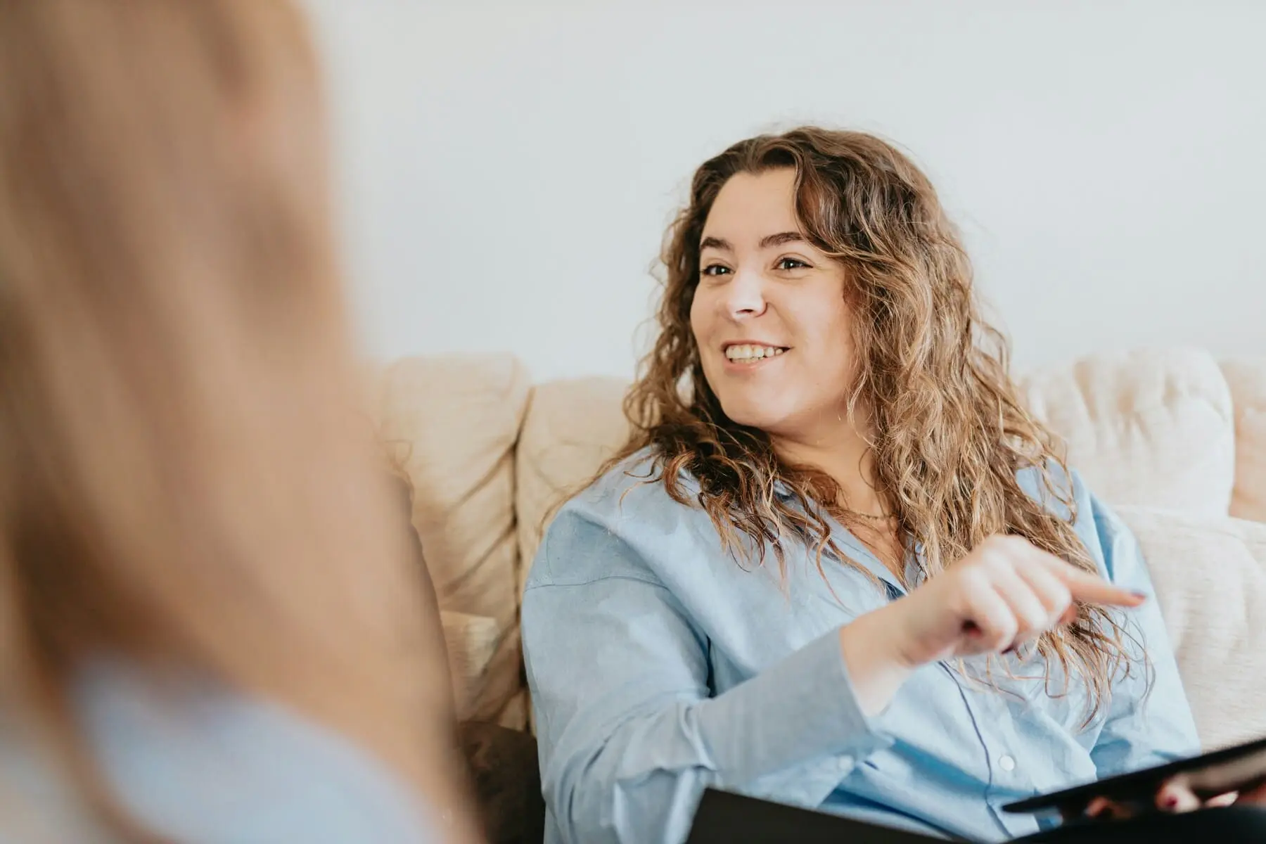 Woman sitting comfortably on a couch, talking to someone and looking happy.