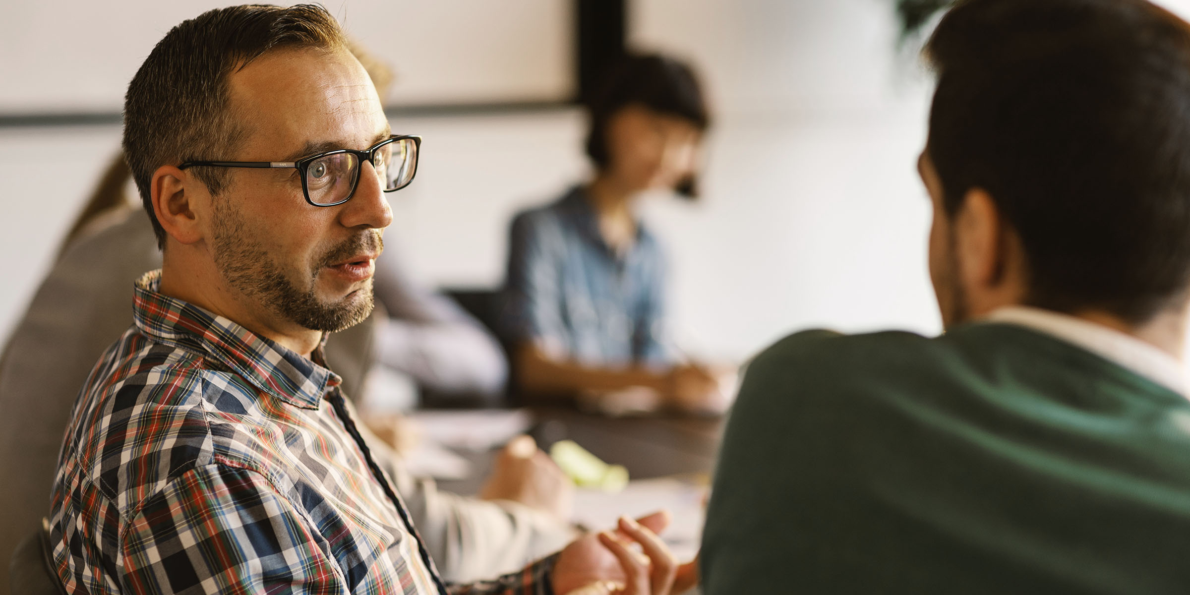 Man in glasses talking to another person around a large meeting table