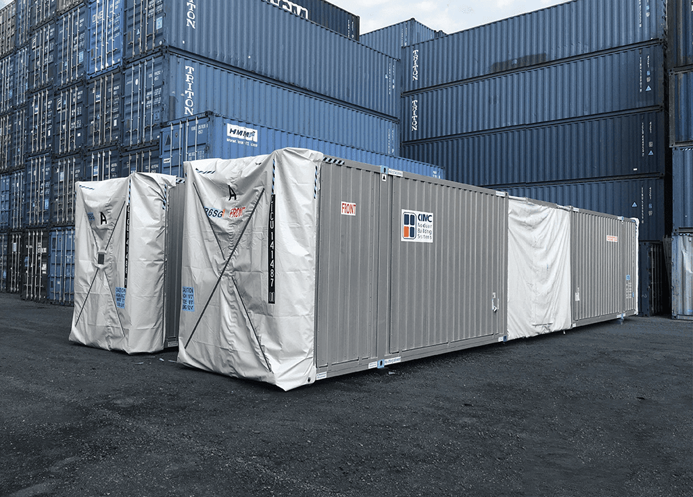 Two corrugated metal hotel guestroom modules shown amongst a yard of typical shipping containers.