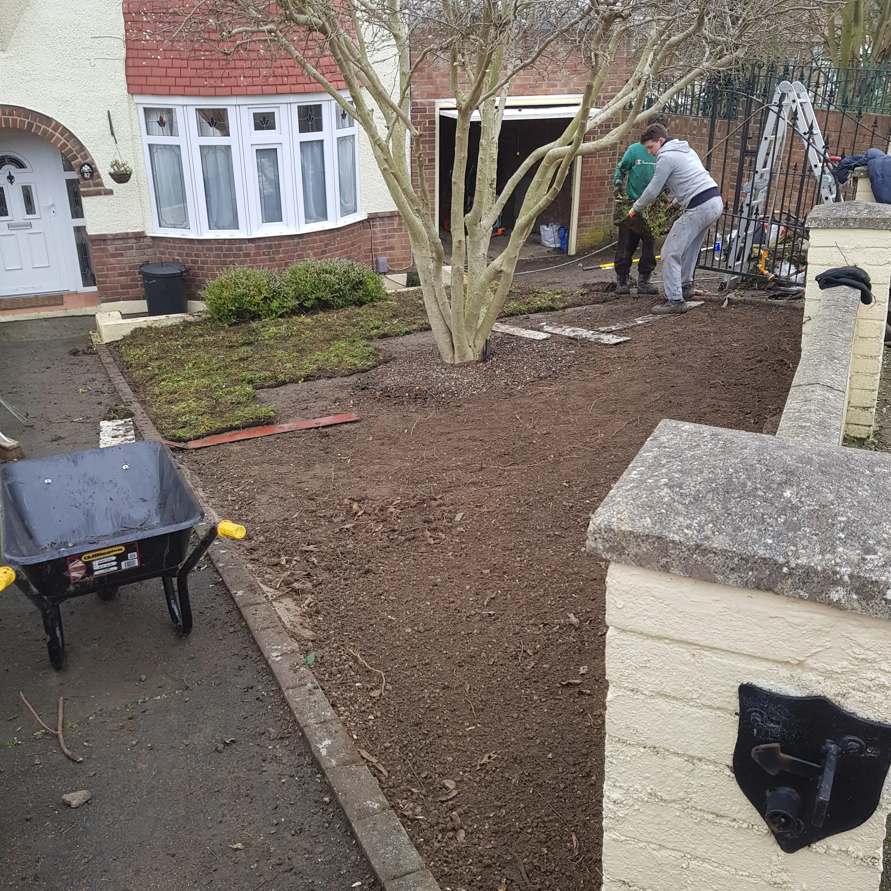 A garden under renovation, with a wheelbarrow and people working on landscaping.