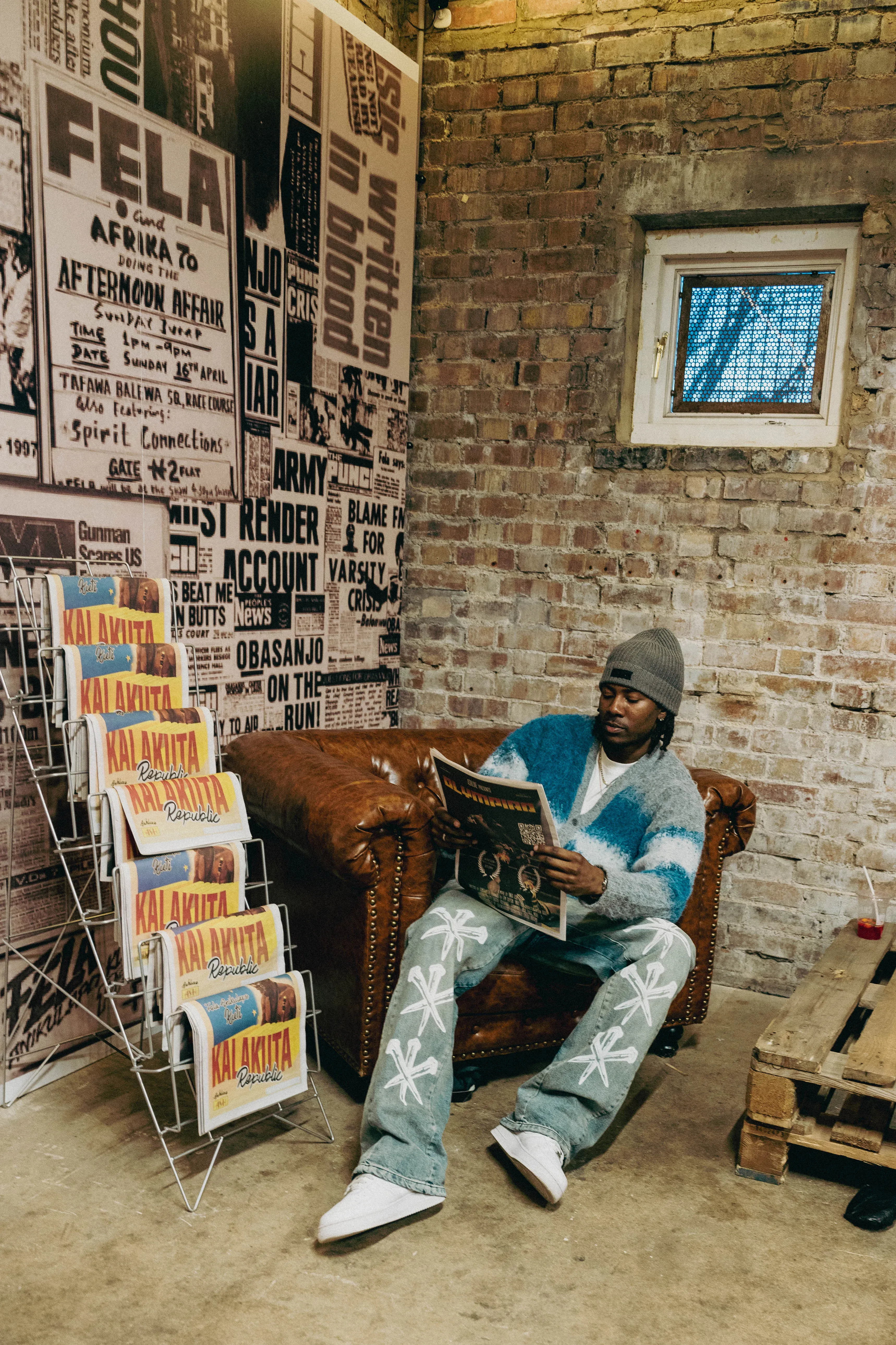 Ashluxe Model sits on a wooden bench, reading in a cozy room with stone walls and colorful art on display.