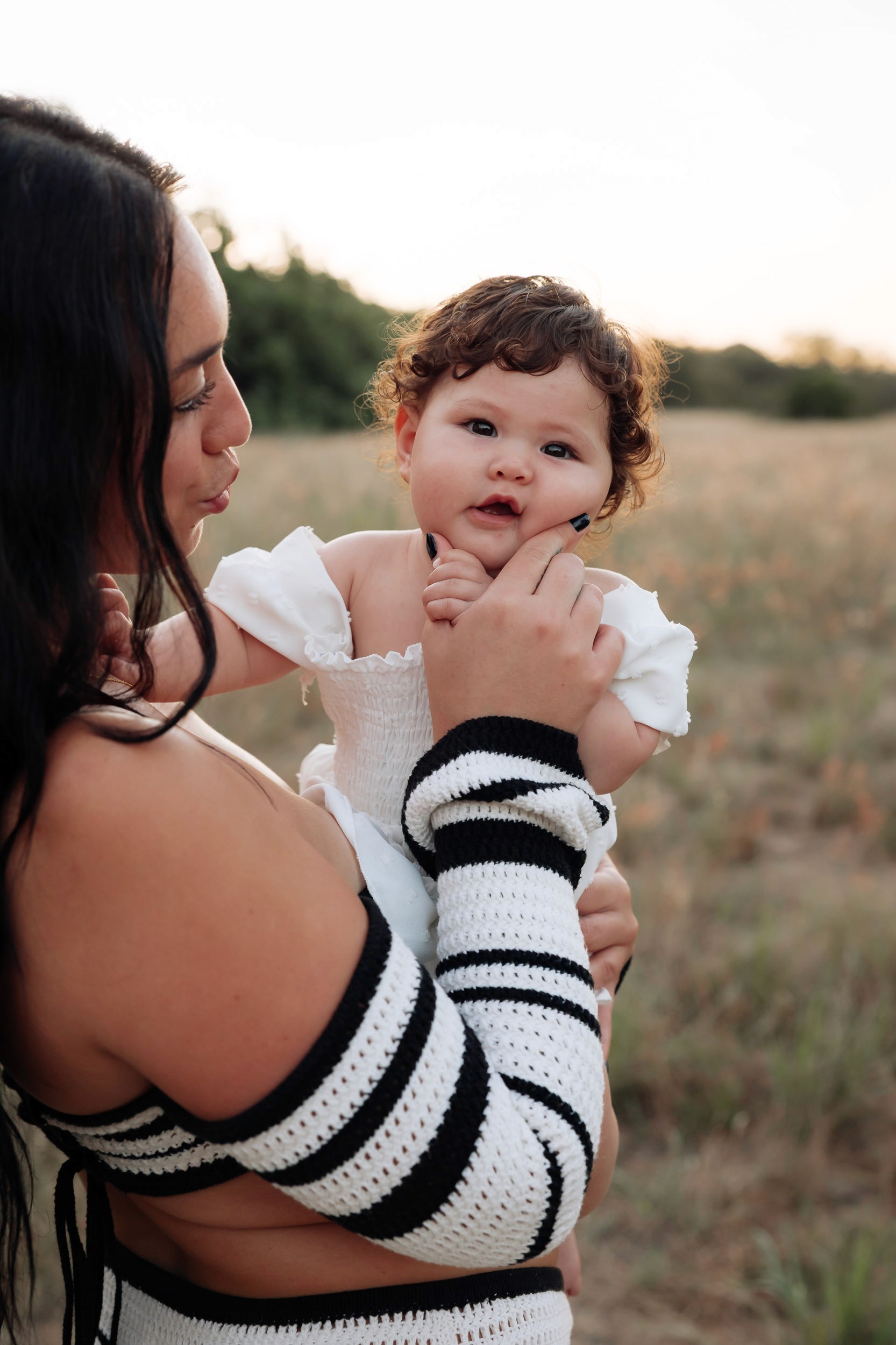 Mother and daughter cuddling in the long grass at sunset during a Mackay motherhood photography session, warm golden light surrounding them.