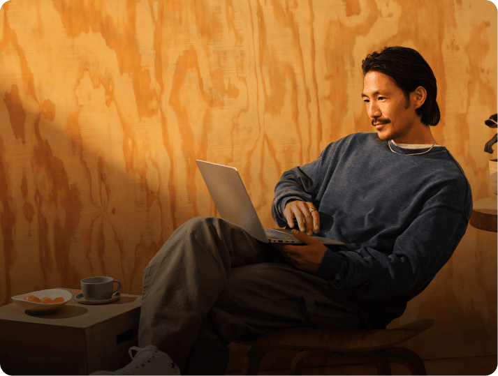 Company name search - Man using laptop, sitting, with coffee and snack on a table, wood wall