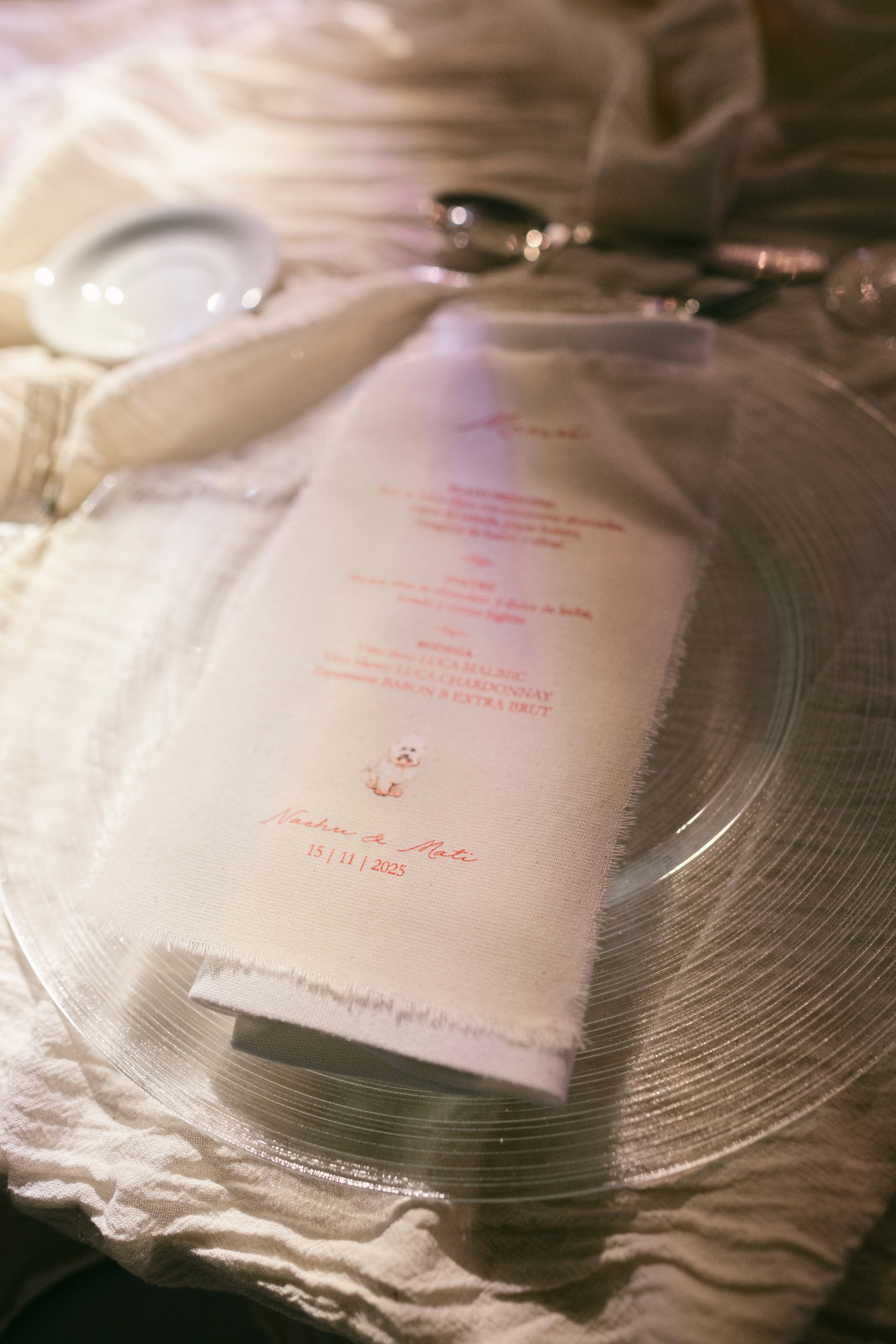 Detalle de cubierto con plato de sitio texturizado y menú de tela deshilachada personalizado.