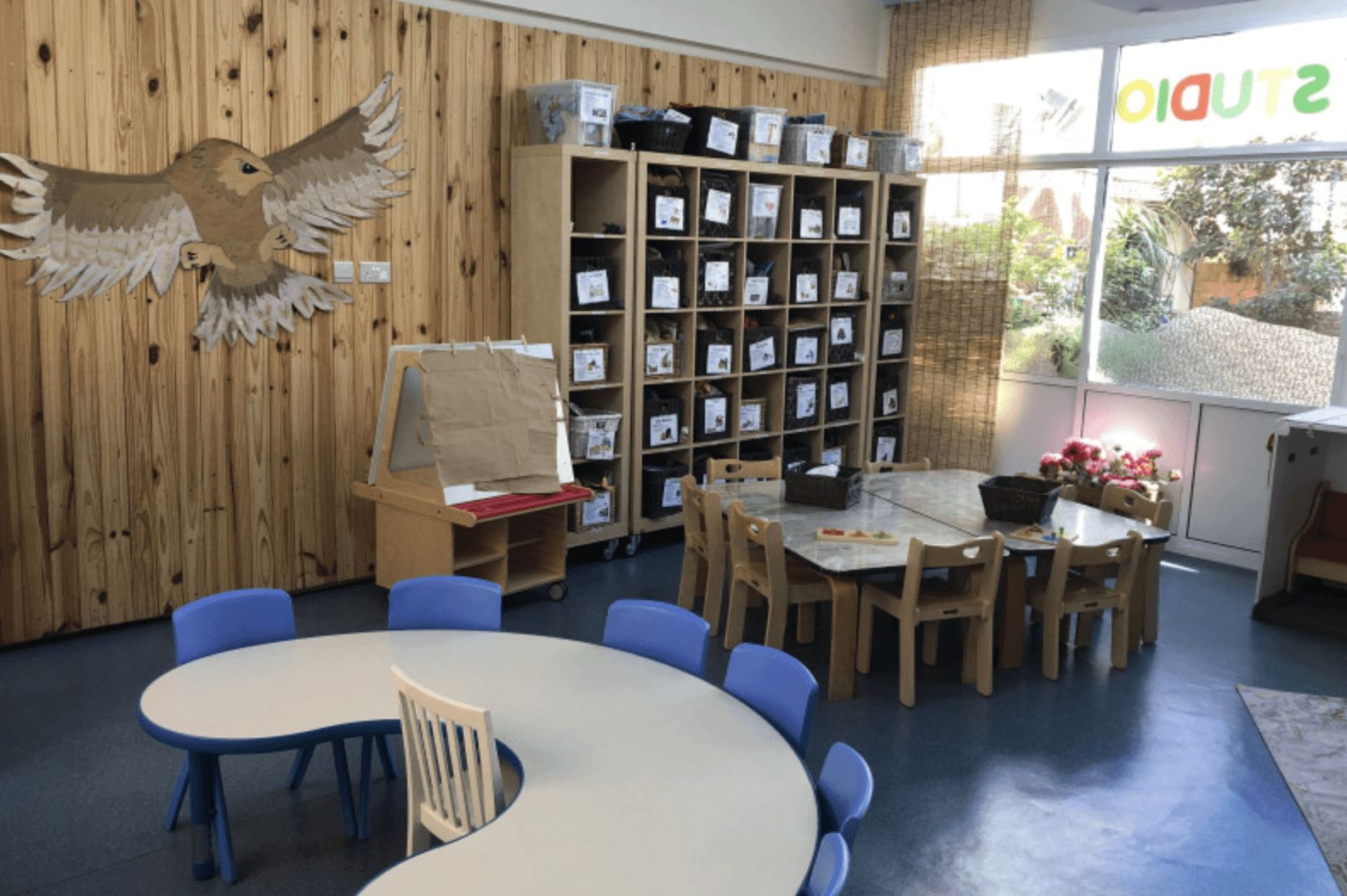 Early childhood classroom with wooden shelves, small tables and chairs, and creative learning materials arranged in a bright indoor space.