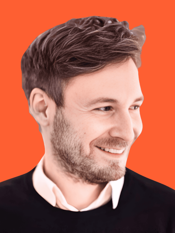 A smiling woman with her arms crossed, standing against a dark green background. She has long, dark hair.