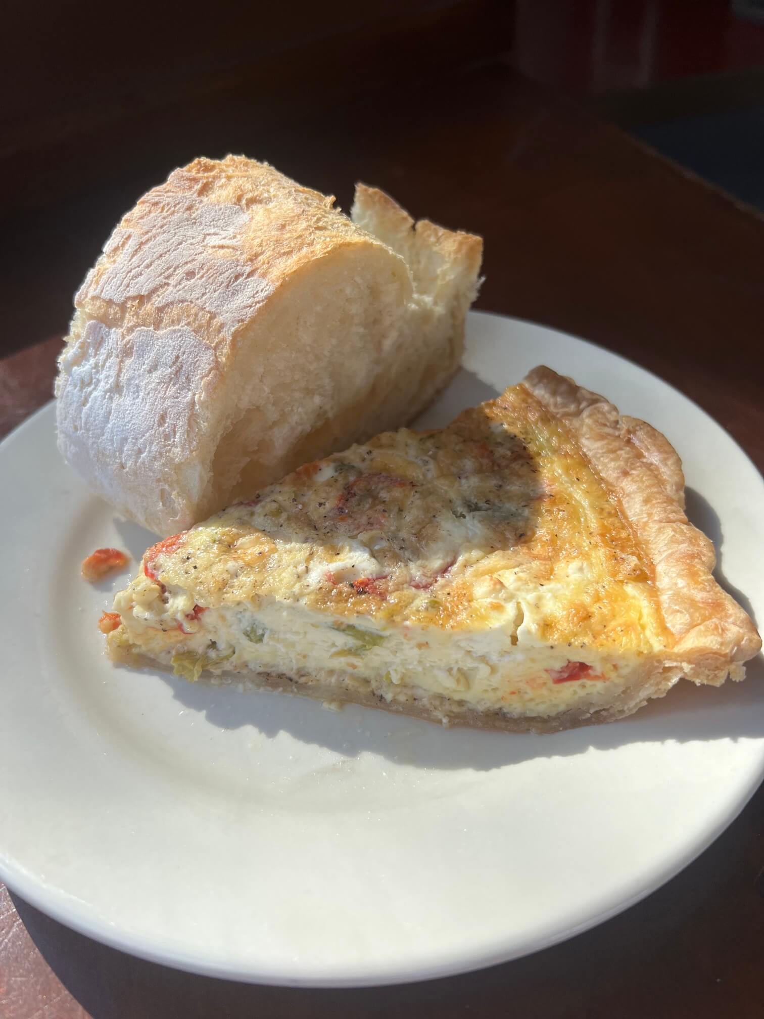 A wedge of quiche beside a piece of crusty bread on a white plate.