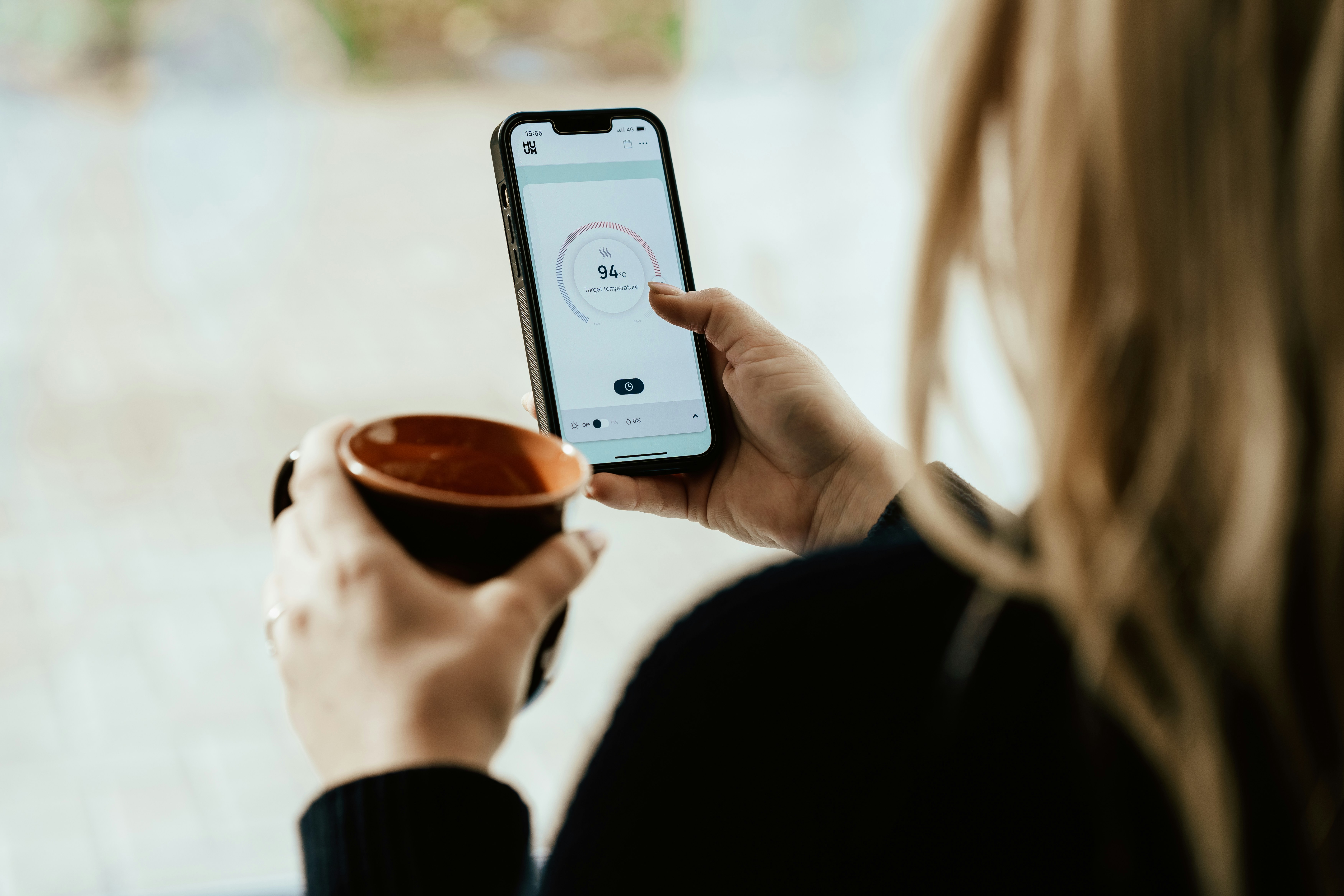 Eine Person, die eine Tasse Kaffee hält und am Handy scrollt.